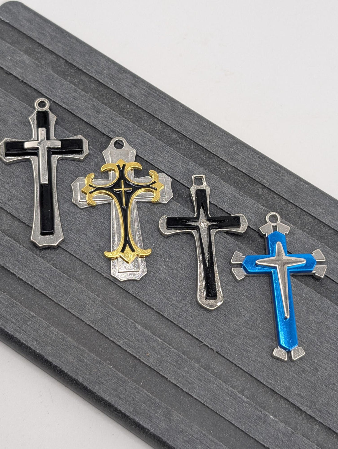 four ornate crosses in various colors and designs, including black, gold, blue, and silver, arranged on a gray surface.