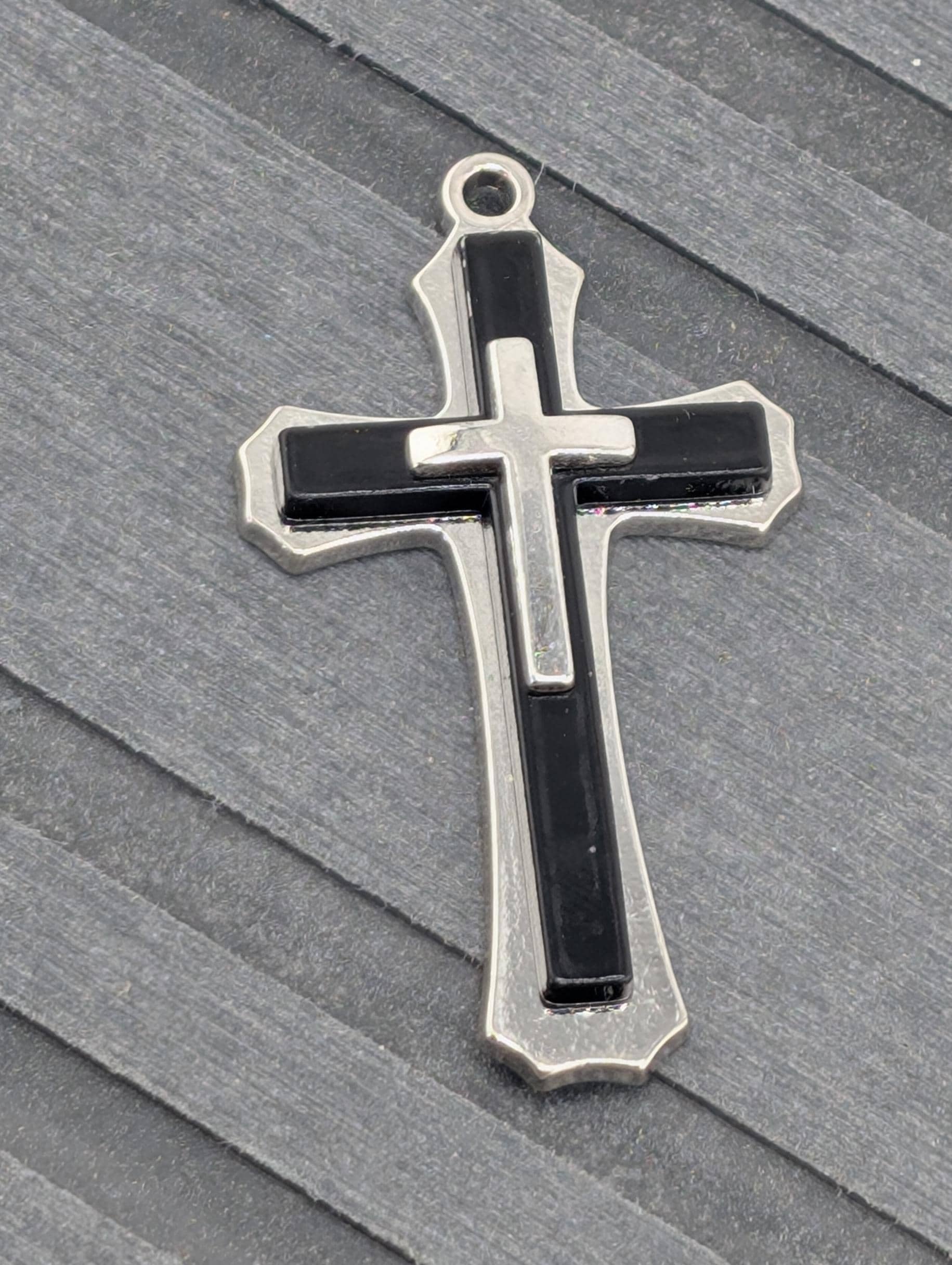A silver and black cross pendant is resting on a grey surface.