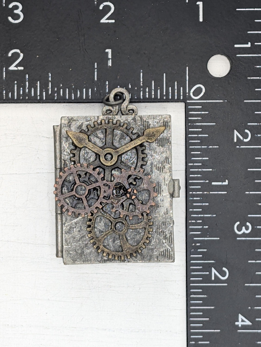 A metal pendant with gears and a ribbon is displayed on a white surface.