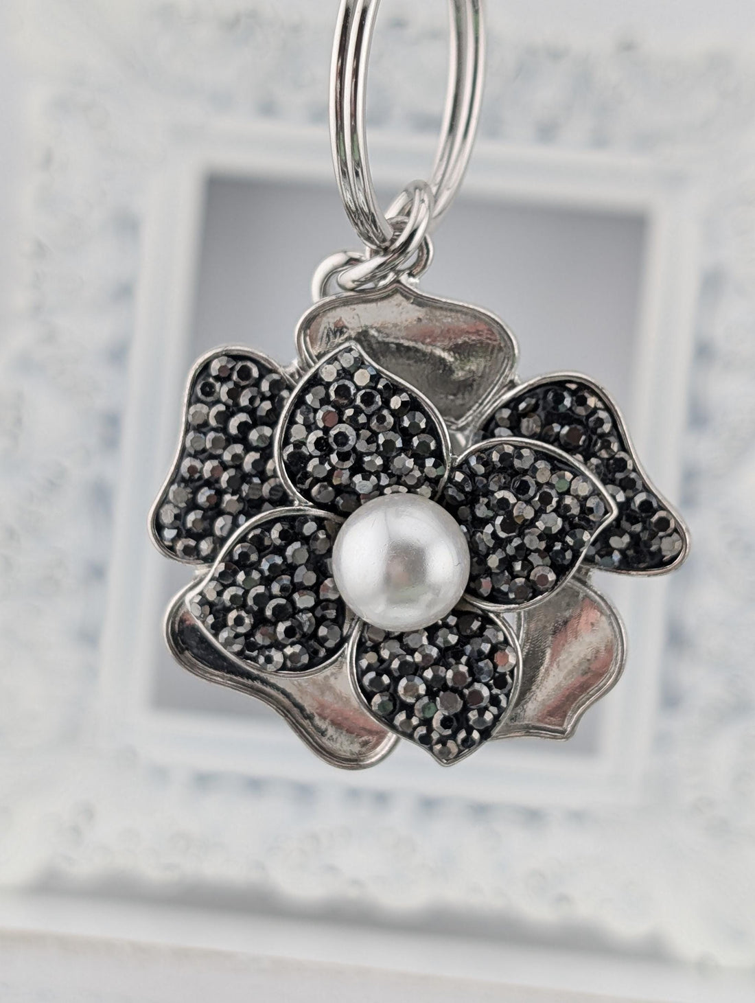 A silver-toned pendant with a large pearl at the center, surrounded by a flower-shaped design with black and white gemstones.