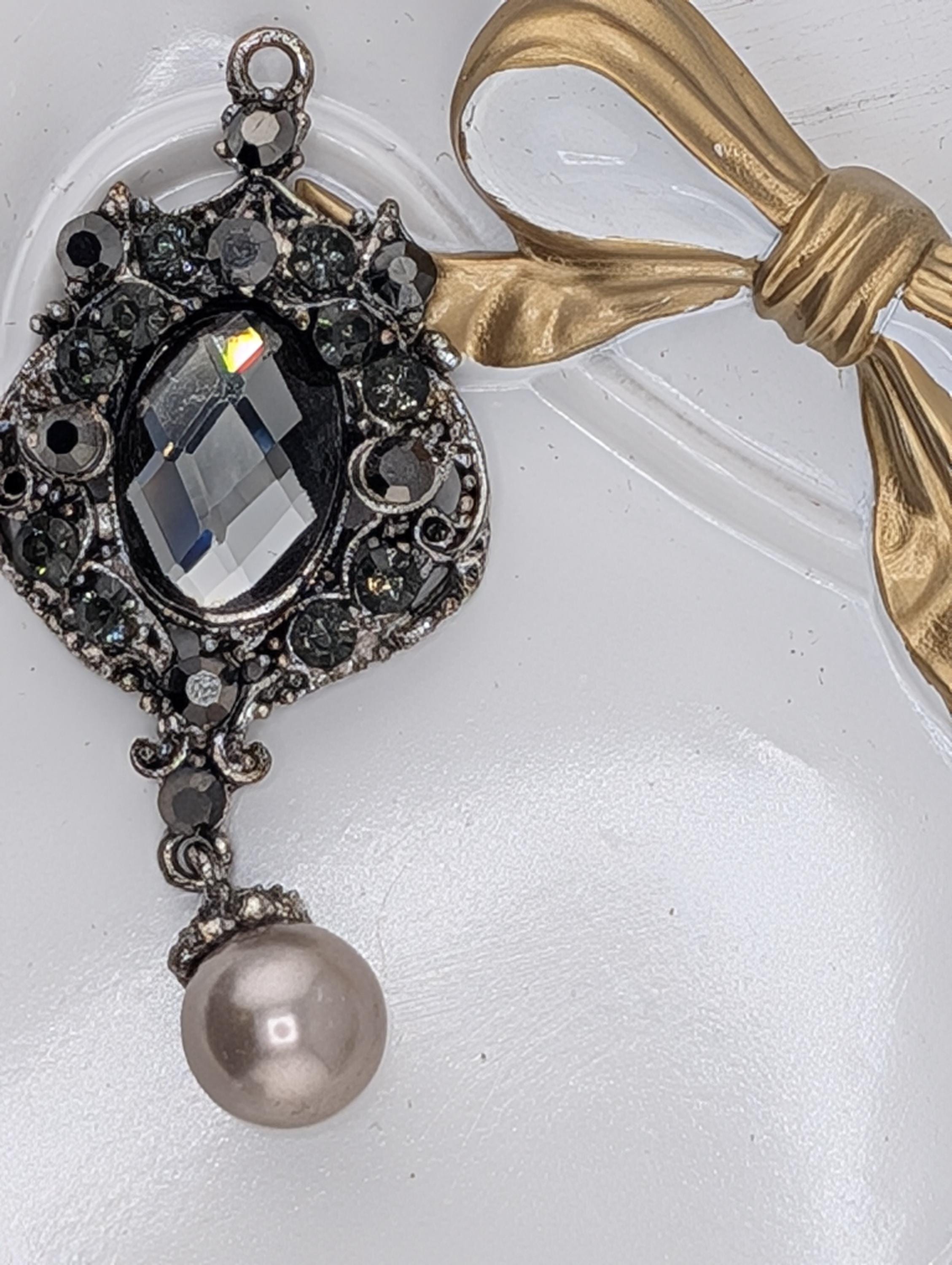 A decorative pendant with a large crystal and a pearl hanging from it, accompanied by a gold ribbon.