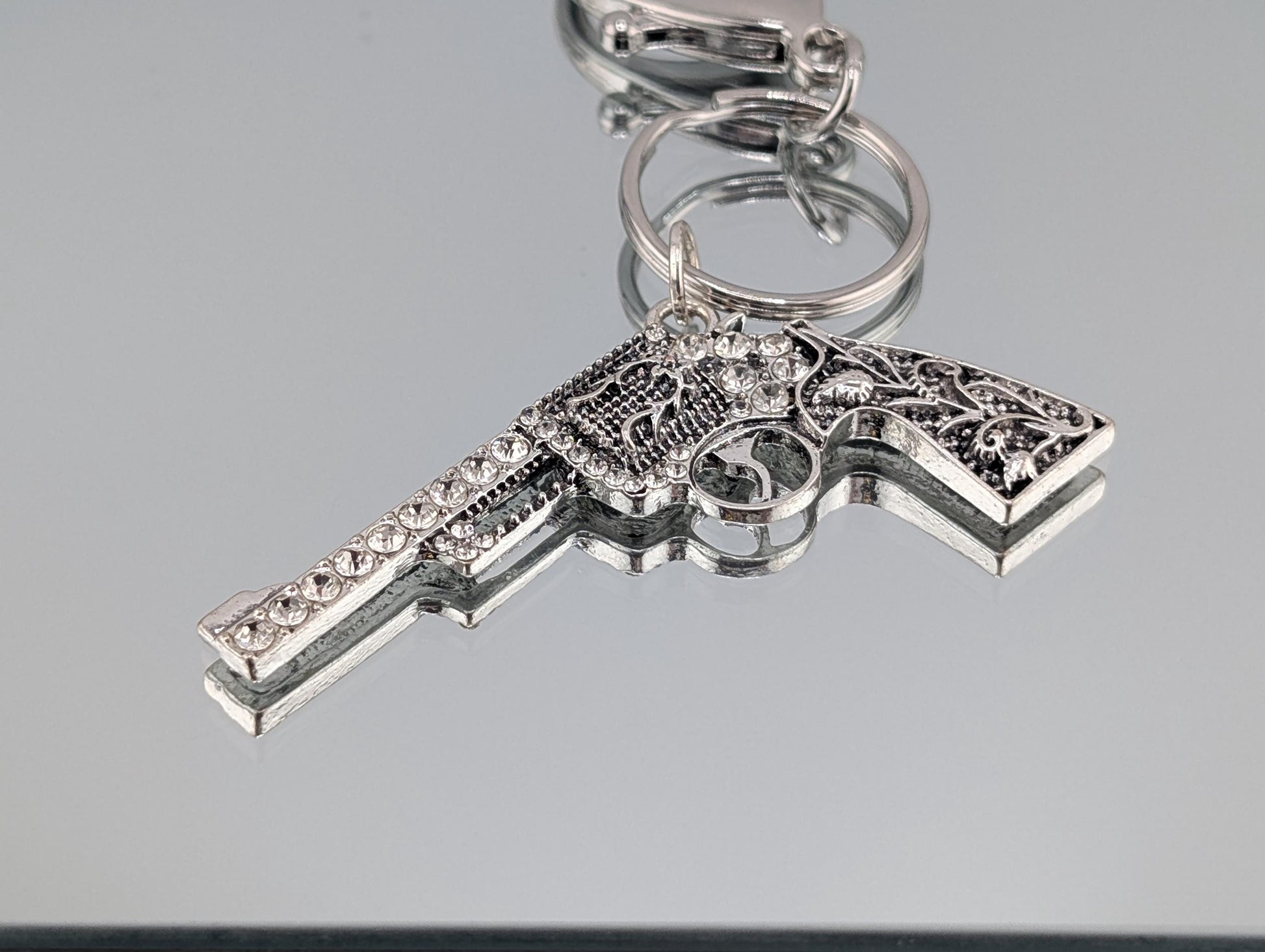 A silver-colored keychain with an ornate, decorative design, including a handle and a trigger mechanism.