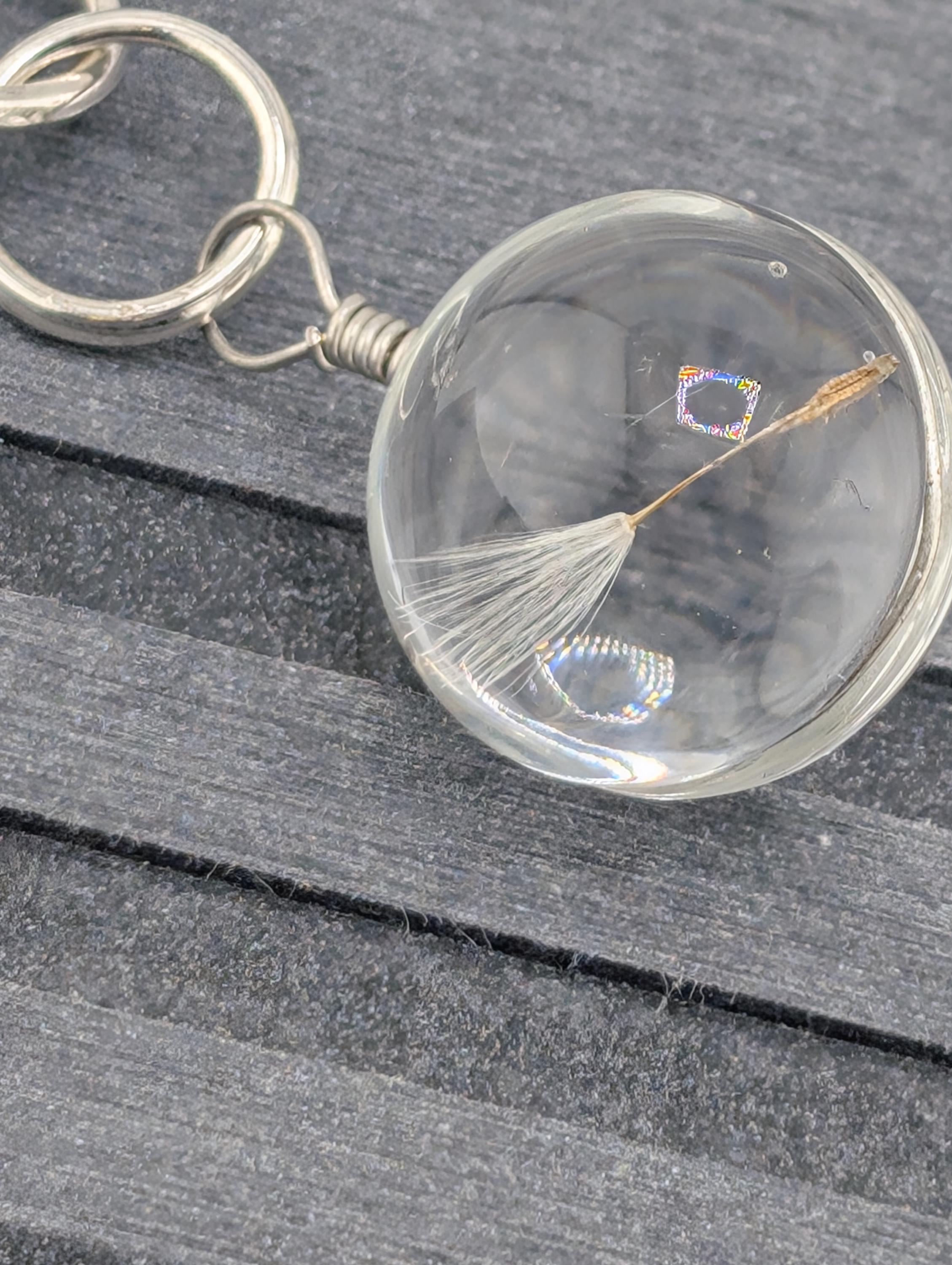 A clear glass keychain with a dandelion seed attached to it, resting on a wooden surface.