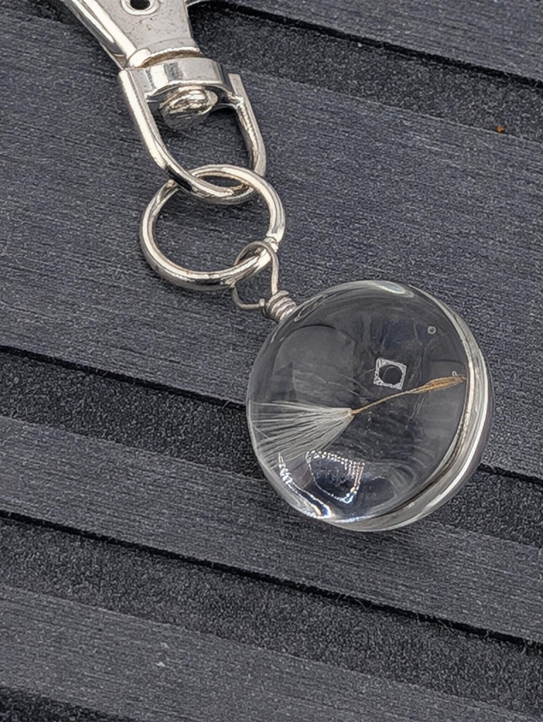A clear glass keychain with a dandelion seed attached to it, resting on a wooden surface.