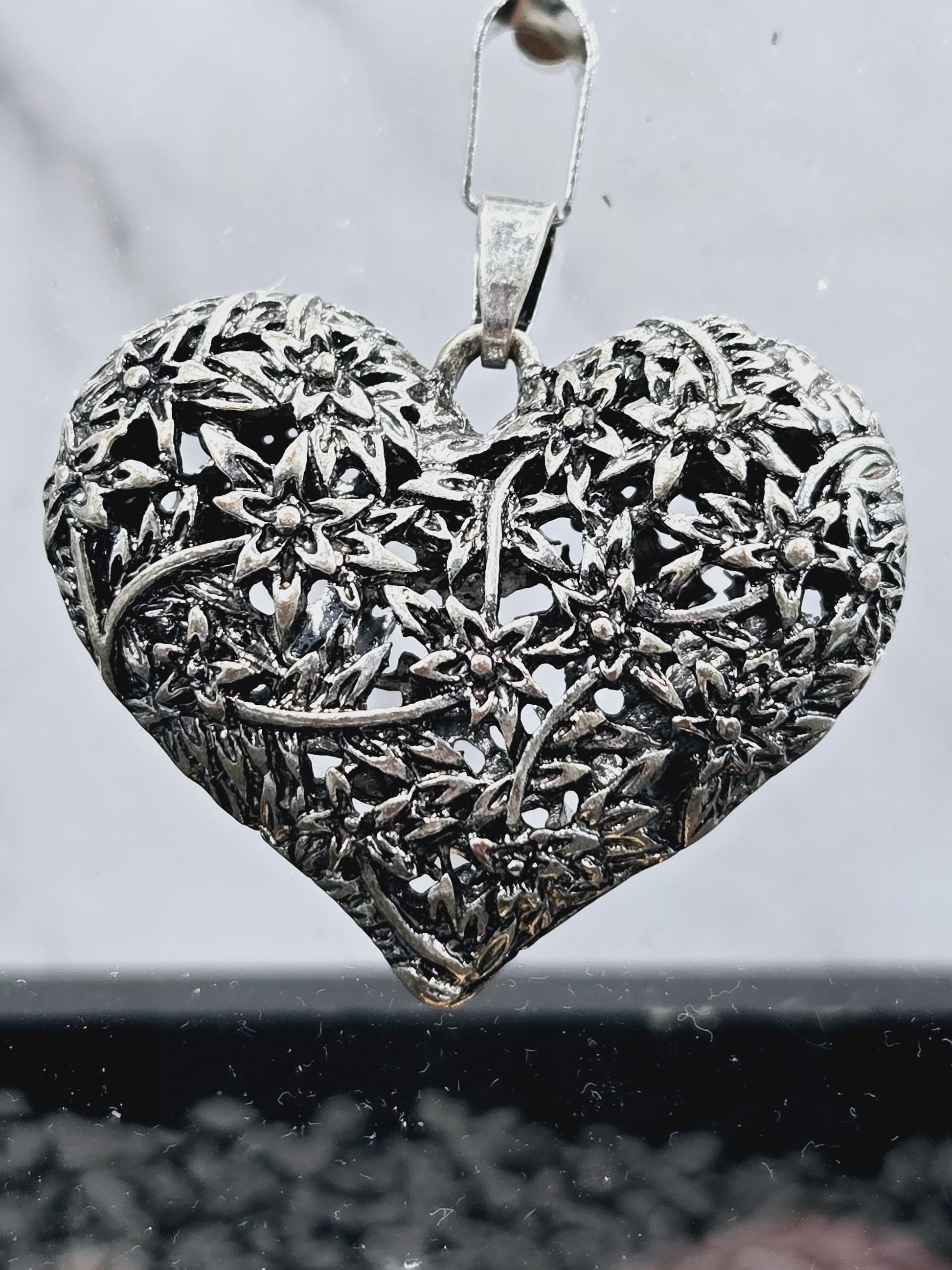 A silver heart-shaped pendant with intricate floral designs.