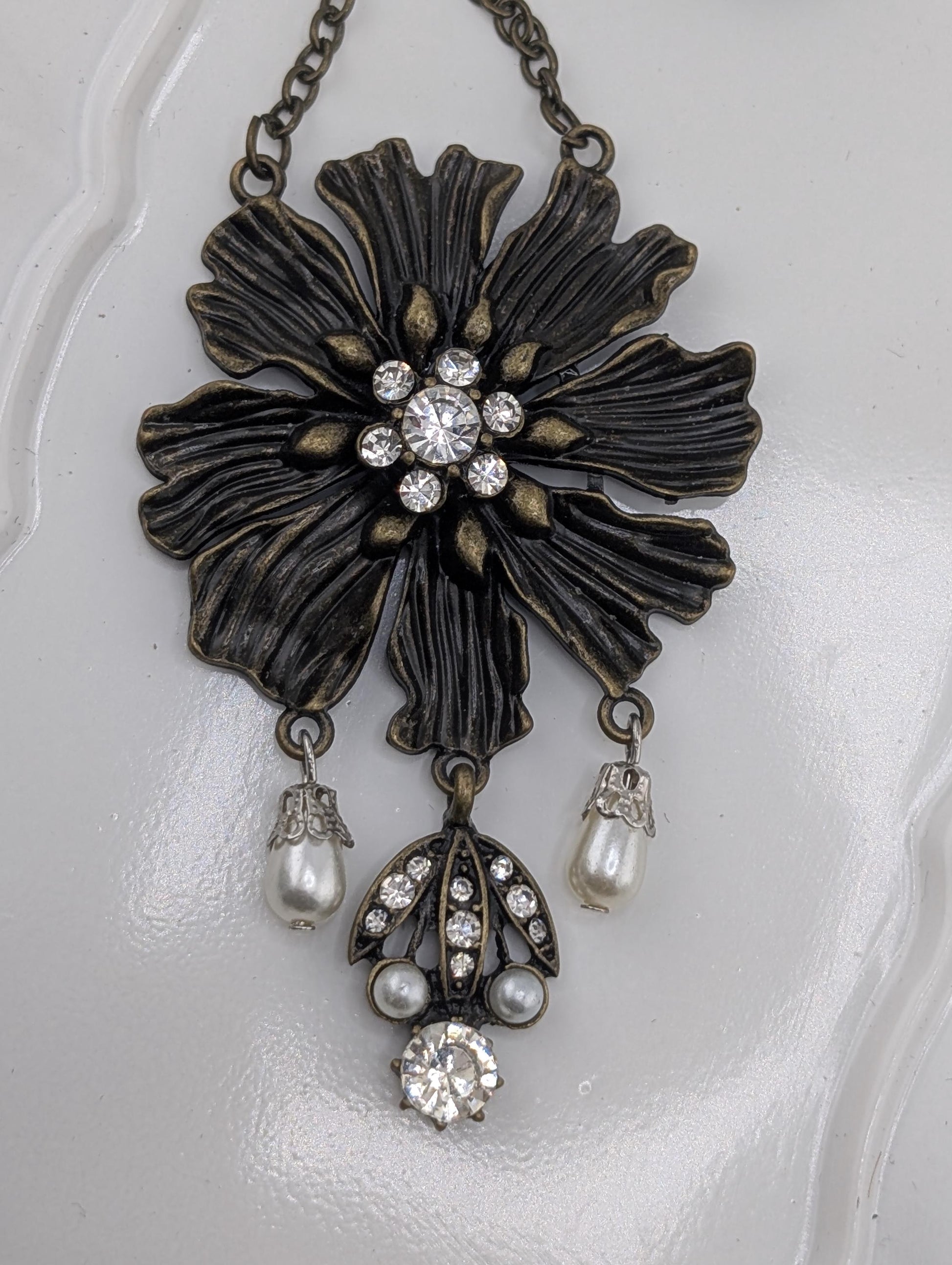 A decorative pendant featuring a large black flower-shaped design with a central crystal surrounded by smaller pearls and diamonds.