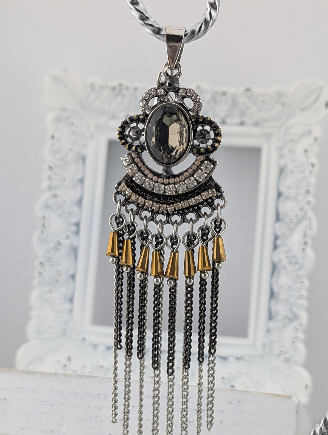 A decorative pendant necklace with a large central stone surrounded by smaller stones and dangling chains.