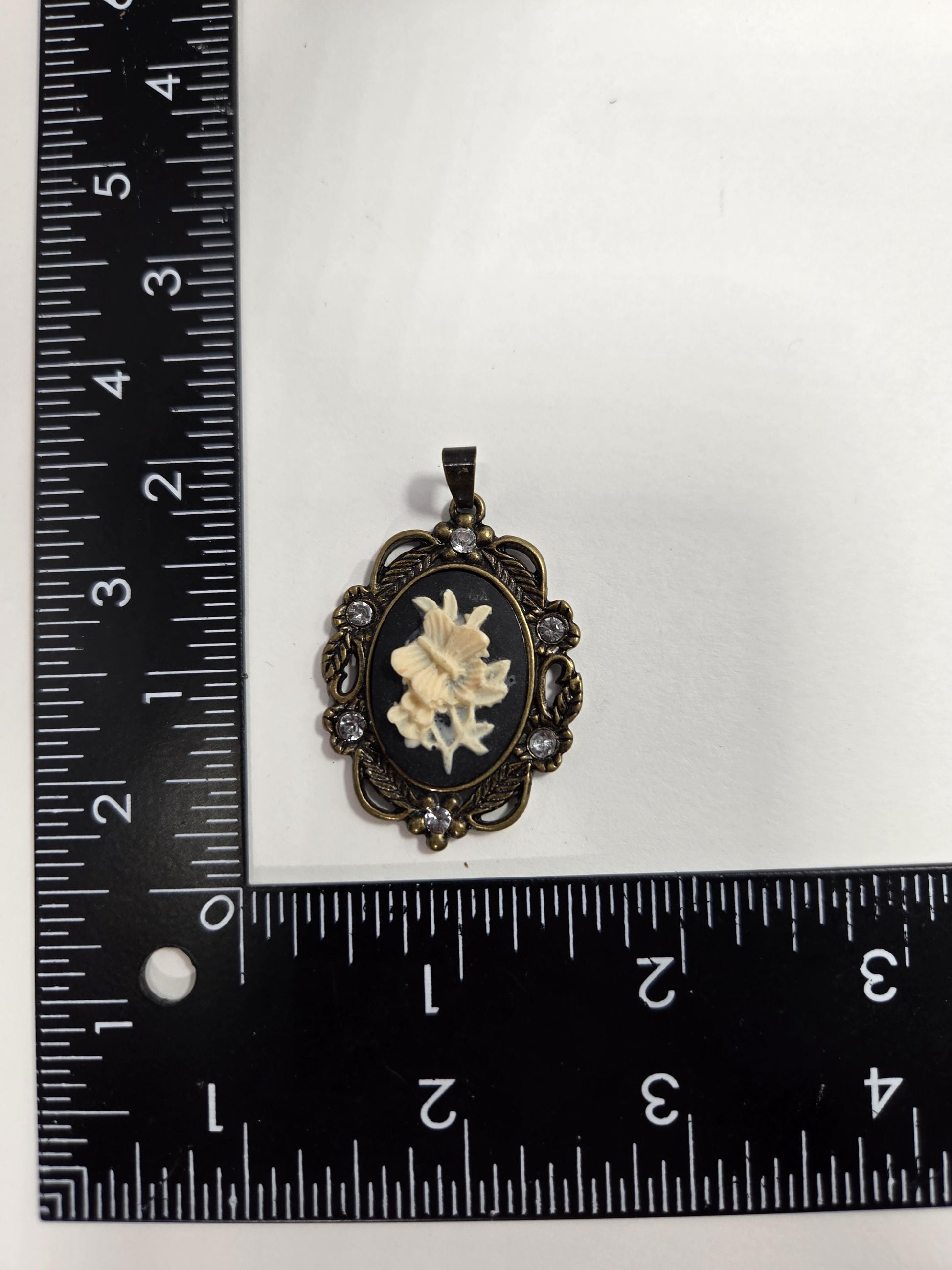 a pendant with a floral design, placed next to a ruler for size comparison.