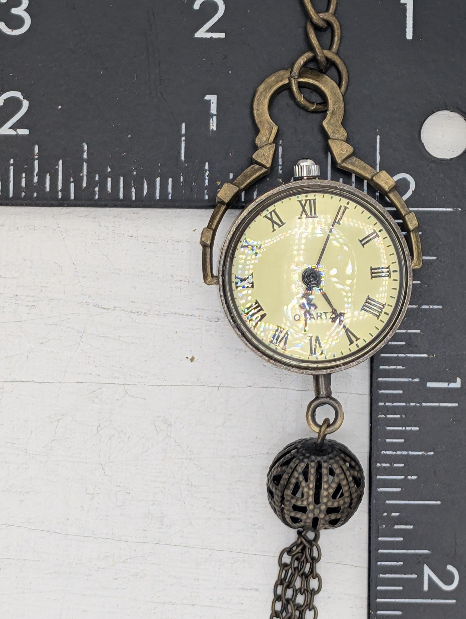 A close-up view of a gold-colored pocket watch with Roman numerals on its face, hanging from a chain.