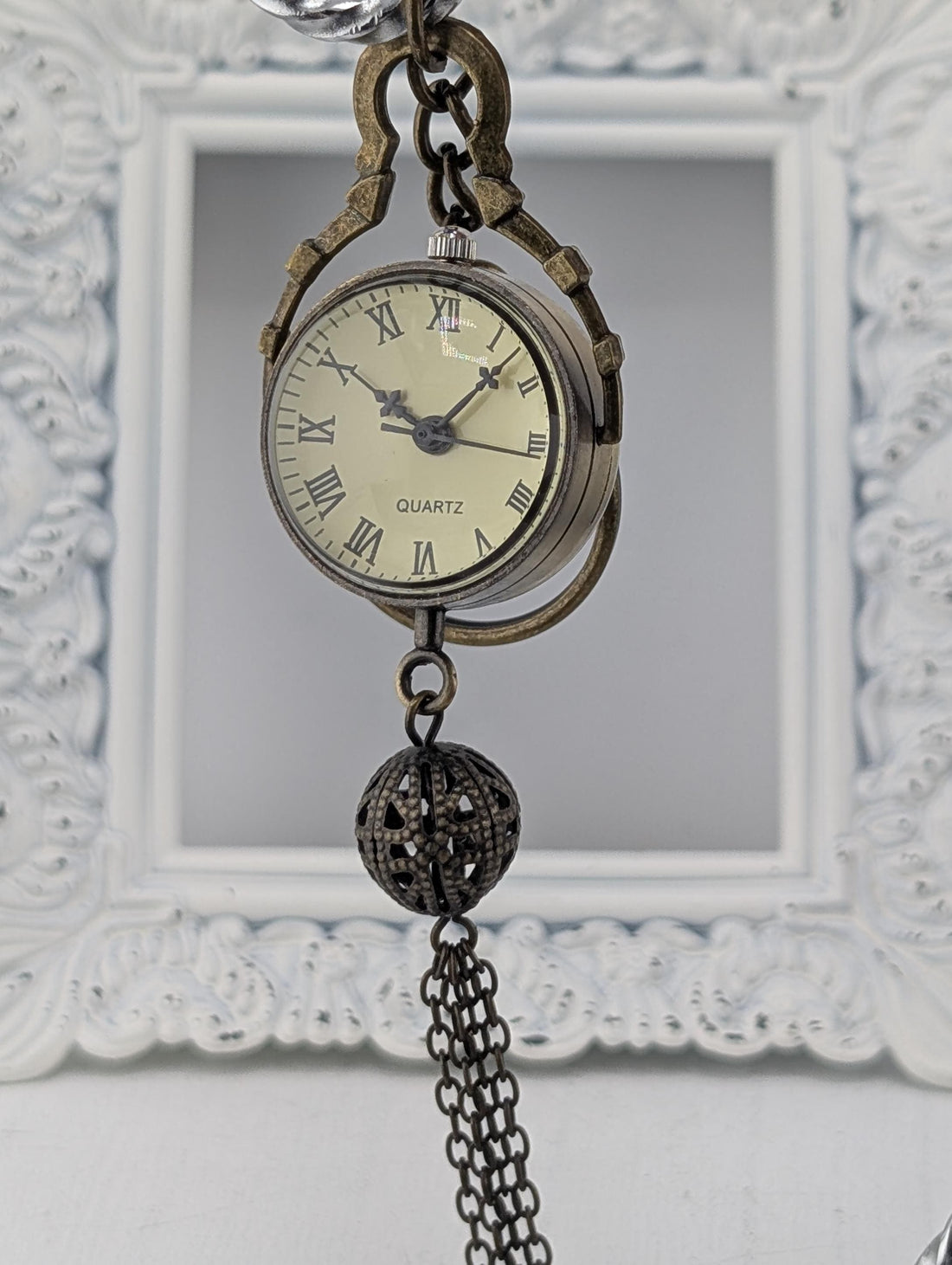 An antique pocket watch with a chain hanging from it, displayed against a white ornate background.
