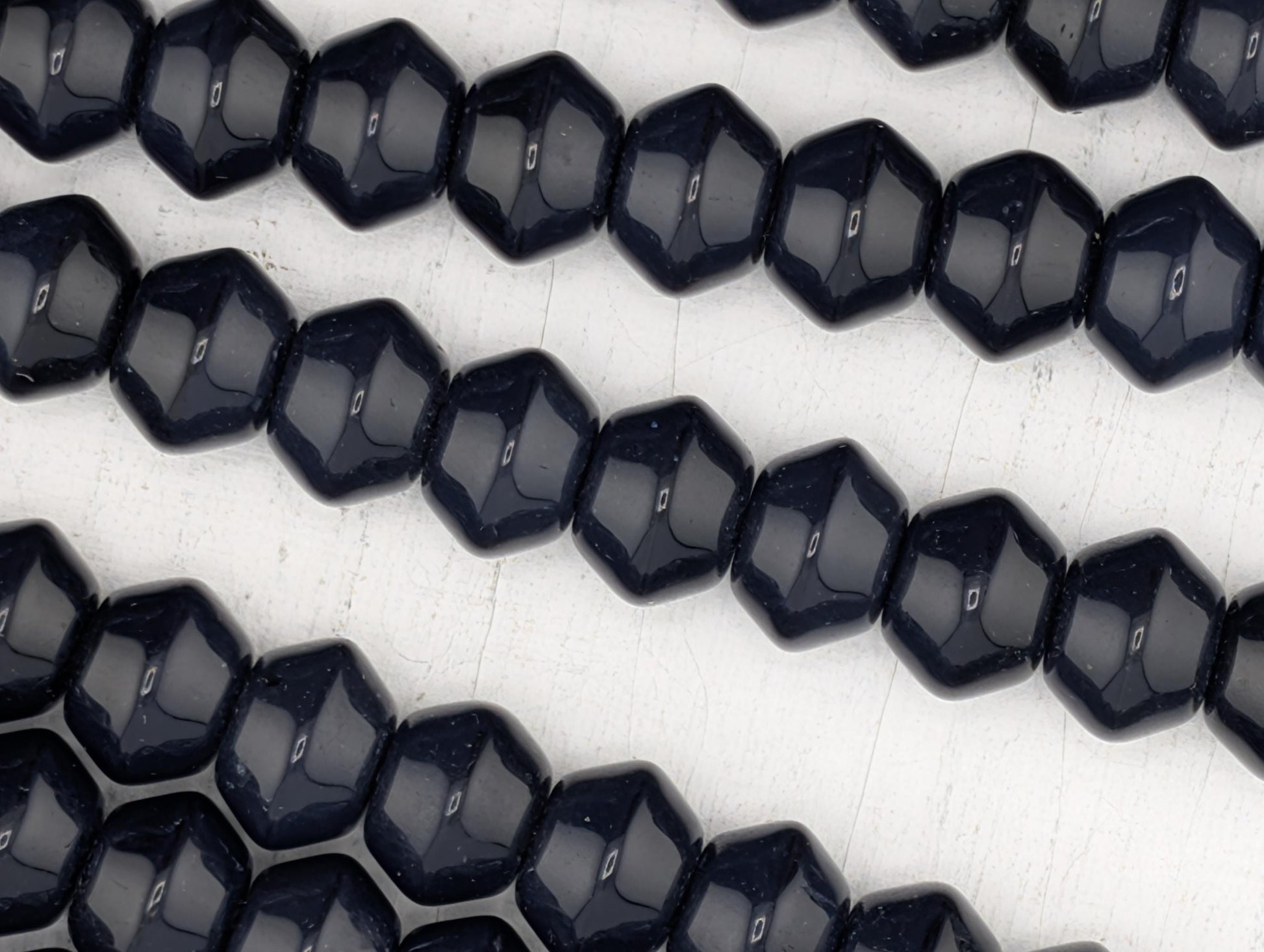 A close-up image of numerous dark blue beads arranged in a repeating pattern on a white surface.