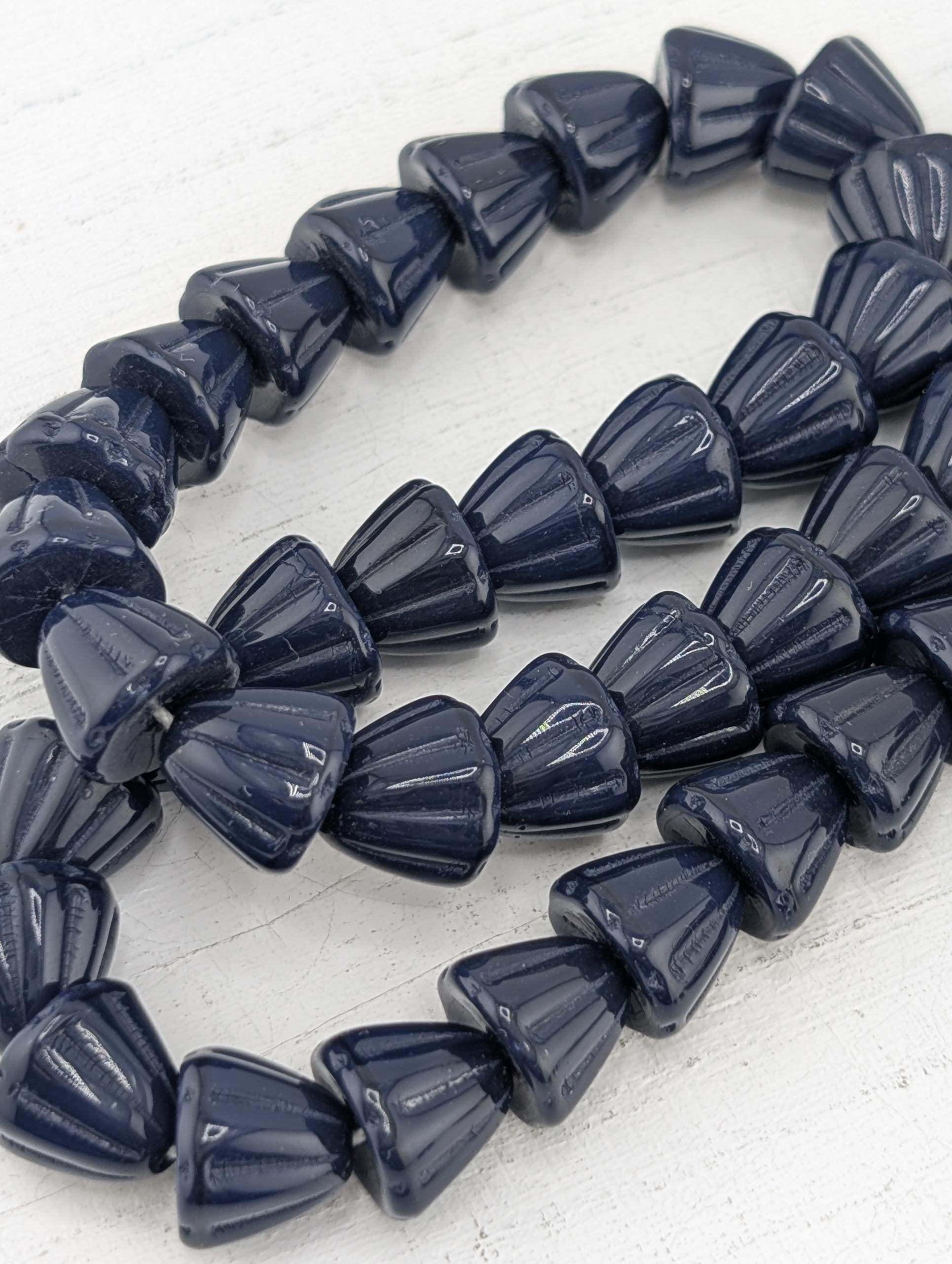 A close-up image of a collection of dark blue, teardrop-shaped beads arranged in a row.