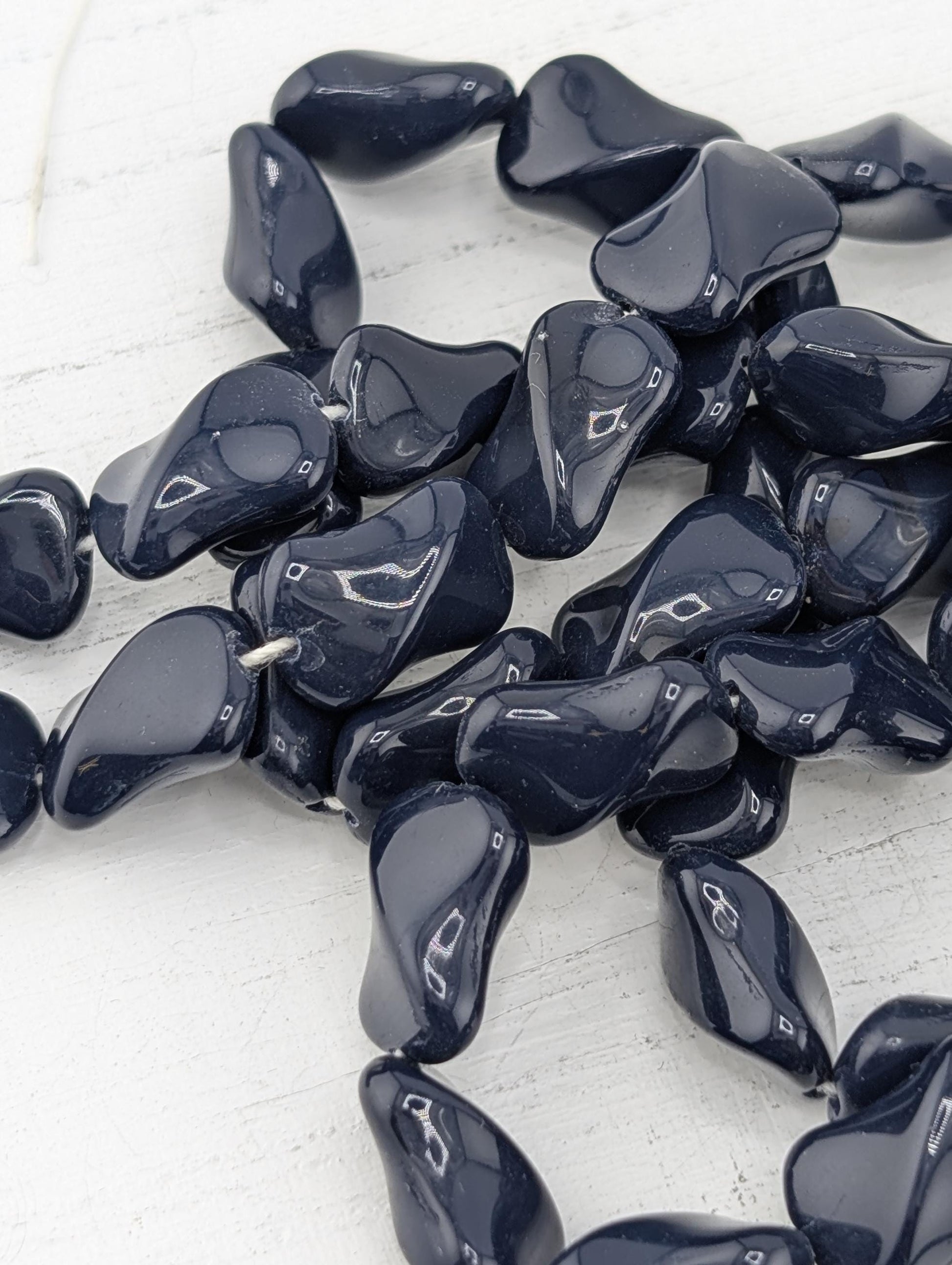 a collection of dark blue, shiny beads or stones arranged on a white surface.
