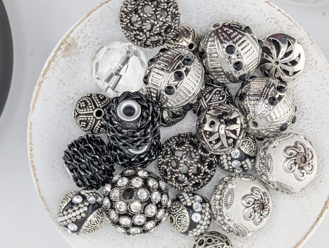 A white plate filled with various decorative beads and charms, including some with intricate designs and sparkling embellishments.