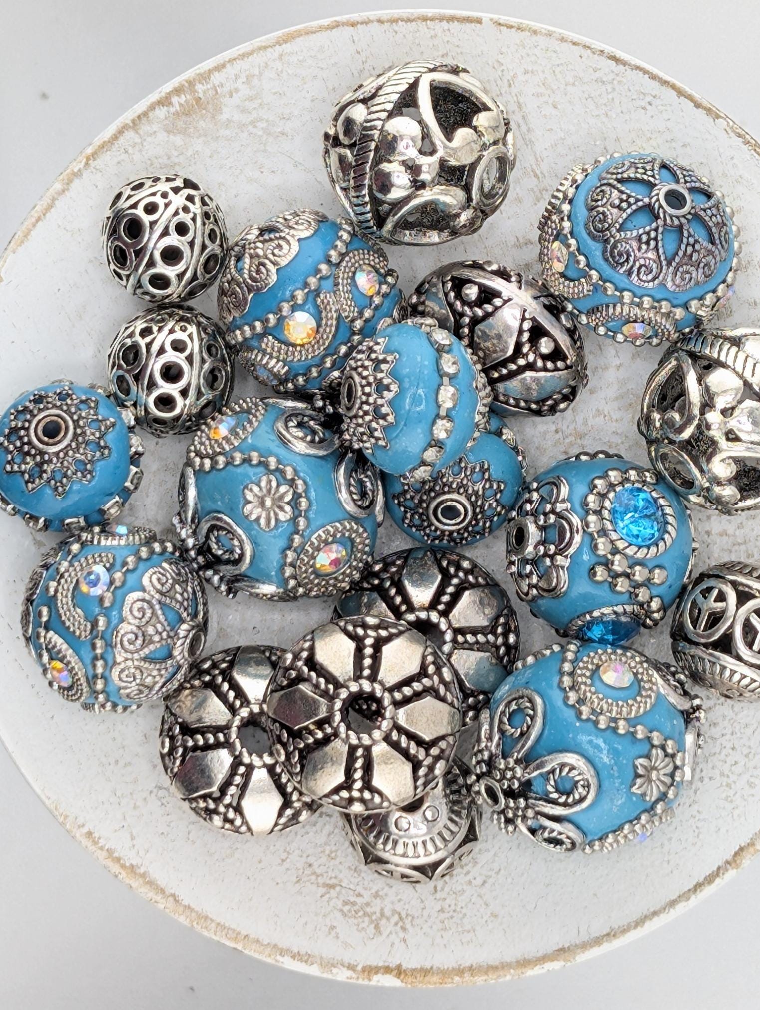 a collection of ornate, blue and silver beads arranged on a white surface.