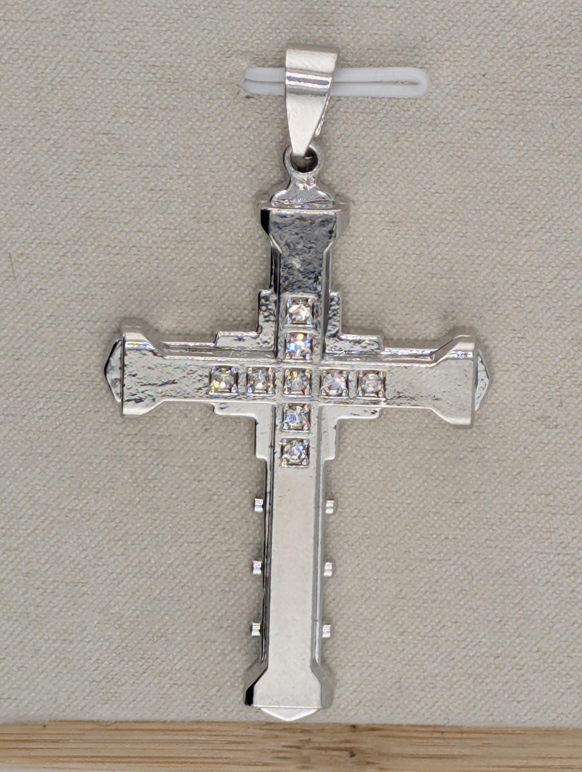 A silver-colored cross pendant with small diamonds or crystals embedded in it, hanging from a metal clasp.