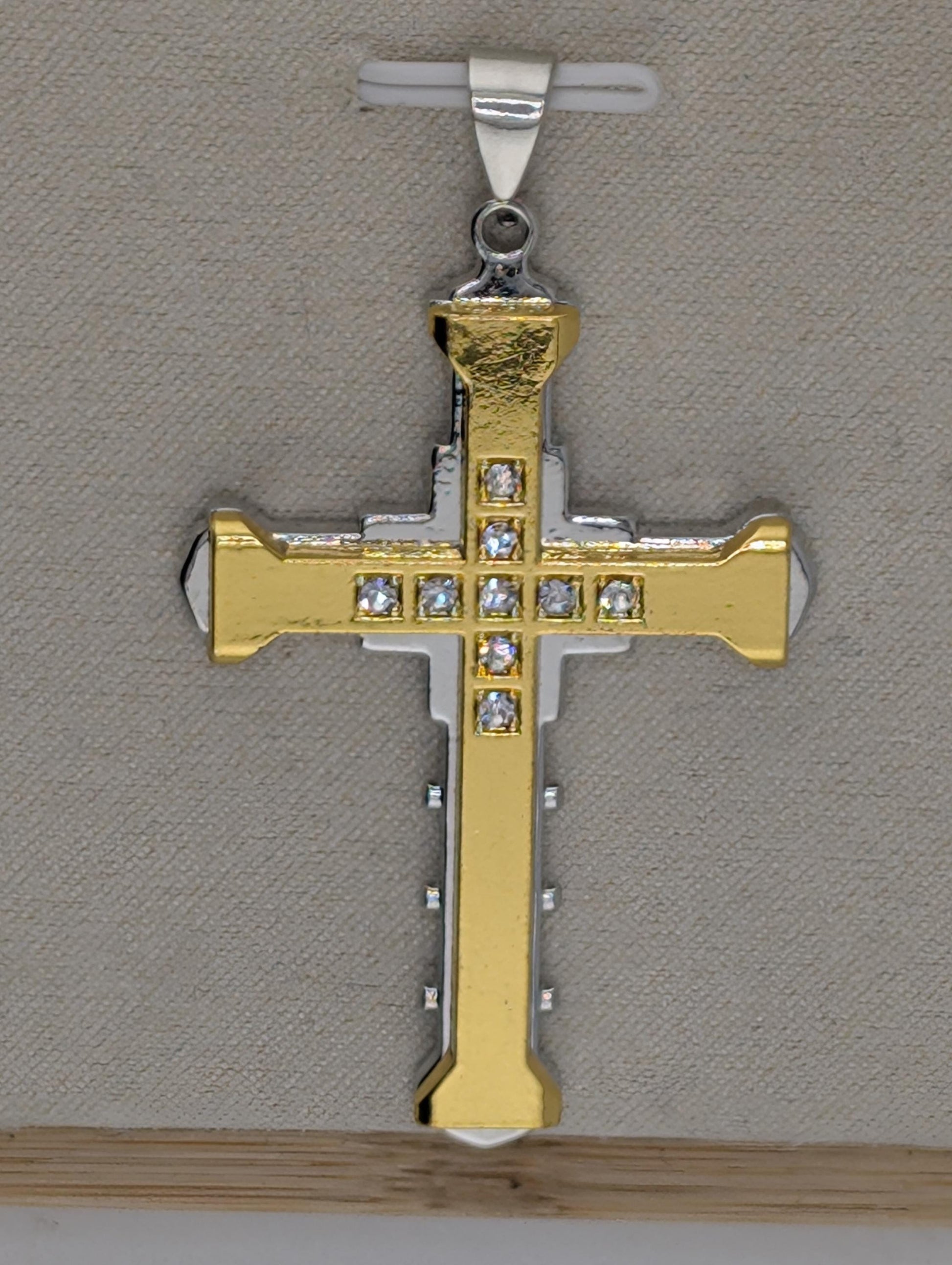 A gold-colored cross pendant with small diamonds or gemstones embedded in it, hanging from a silver clasp.