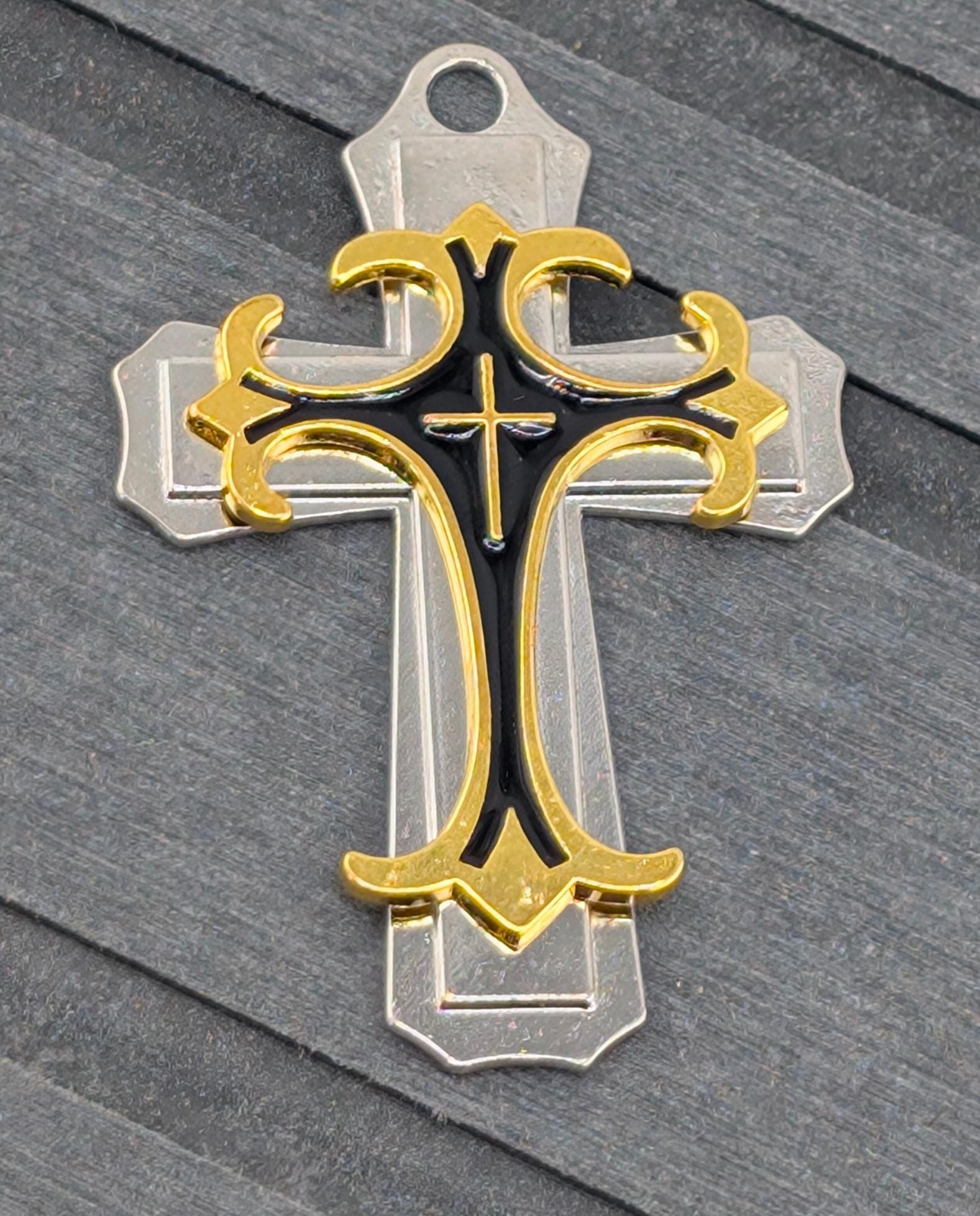A decorative cross pendant with a gold and black design, resting on a gray surface.