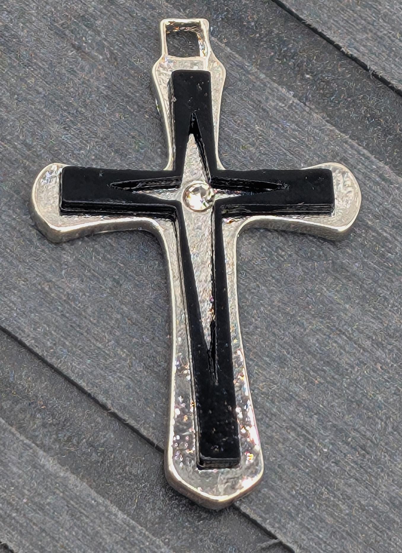 A silver cross pendant with a black cross design is resting on a gray surface.