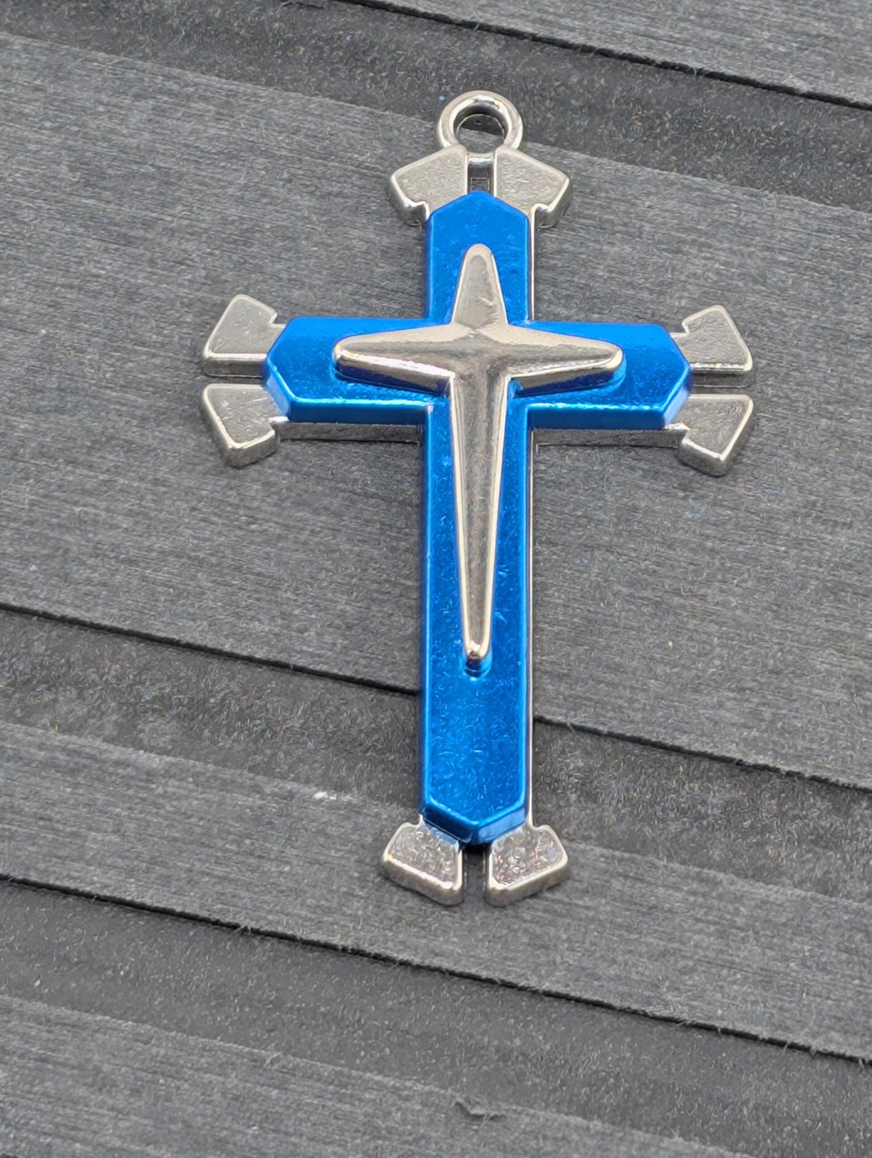 A blue and silver cross pendant is displayed on a wooden surface.