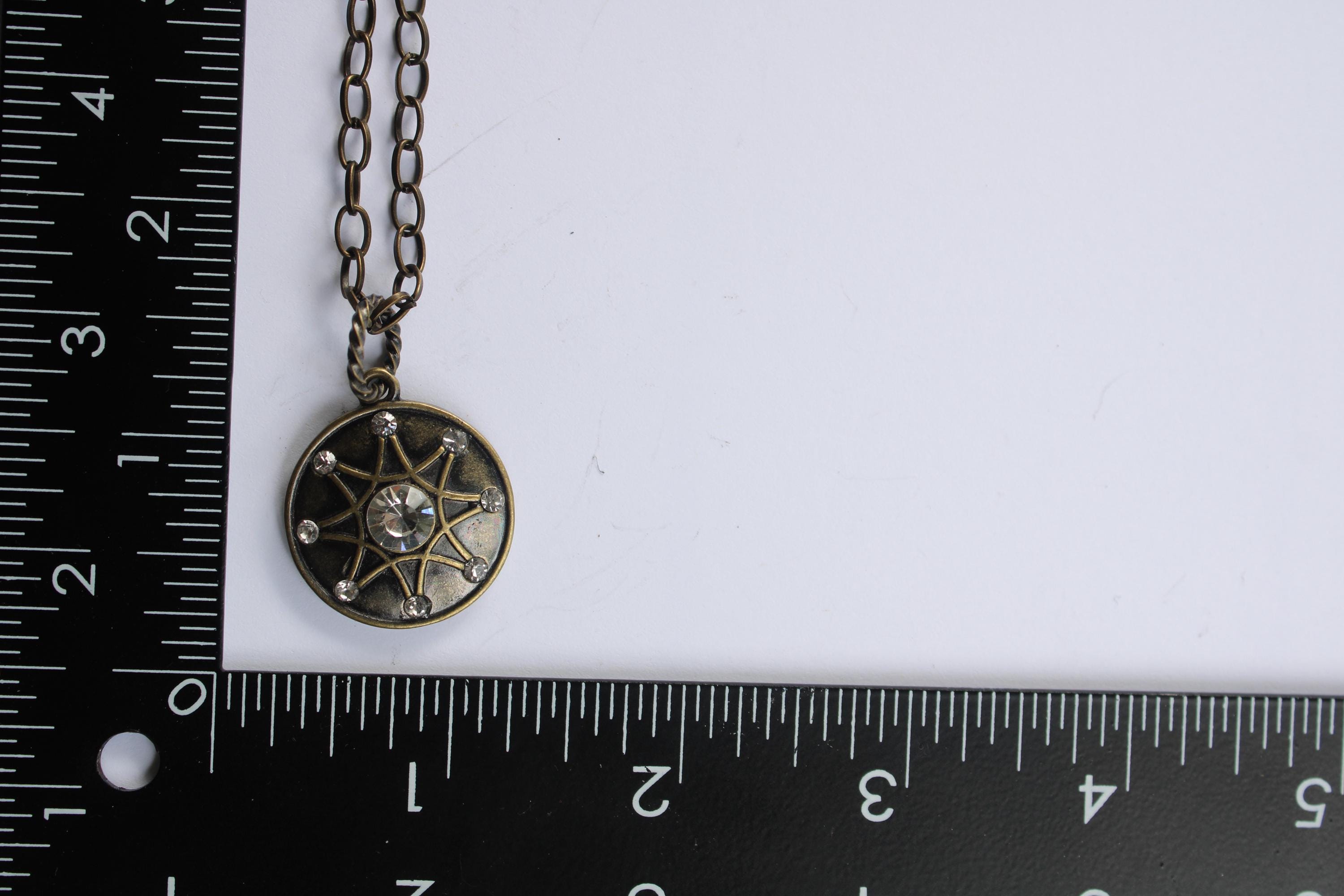A necklace with a pendant is placed next to a ruler on a white surface.
