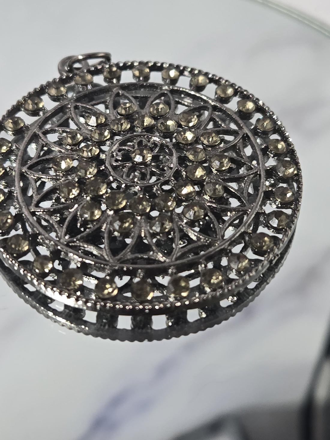 A decorative black metal piece with a circular pattern is displayed in a white wooden box against a marble background.