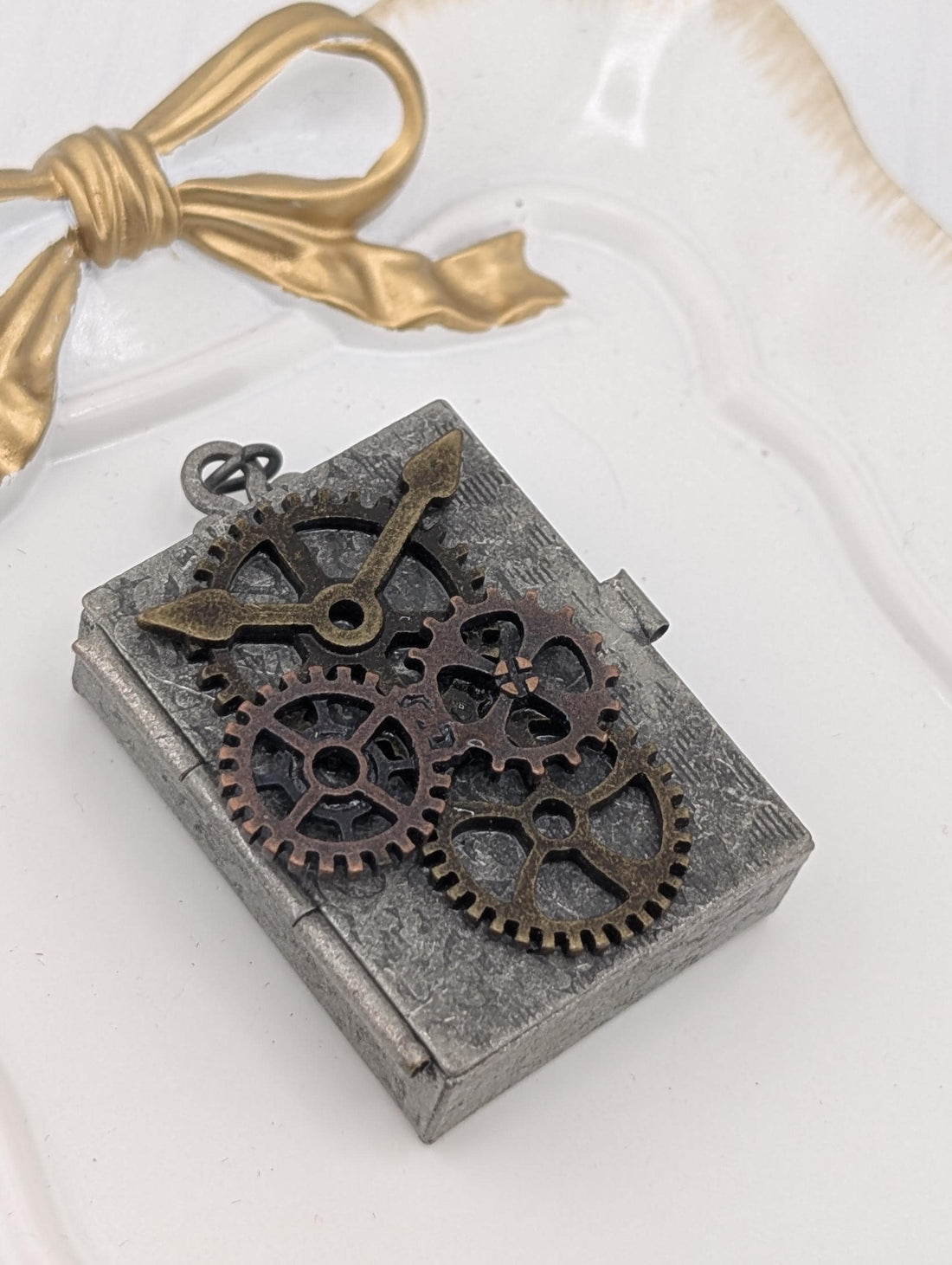 A metal pendant with gears and a ribbon is displayed on a white surface.