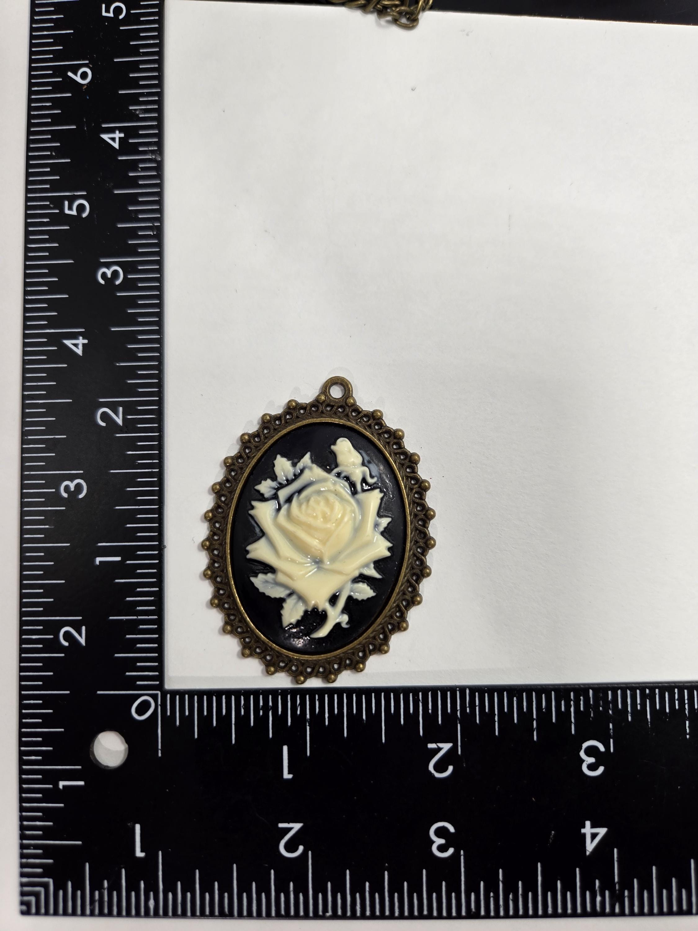 a close-up view of a pendant with a rose design, placed next to a ruler for size comparison.