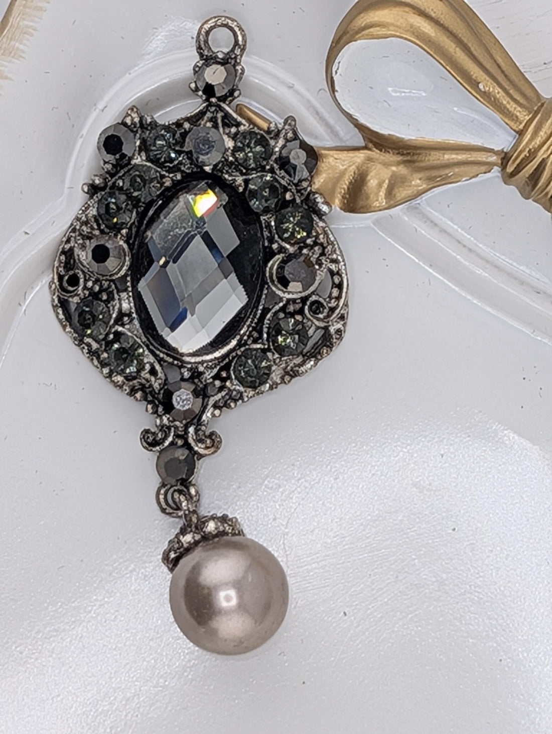 A decorative pendant with a large crystal and a pearl hanging from it, accompanied by a gold ribbon.
