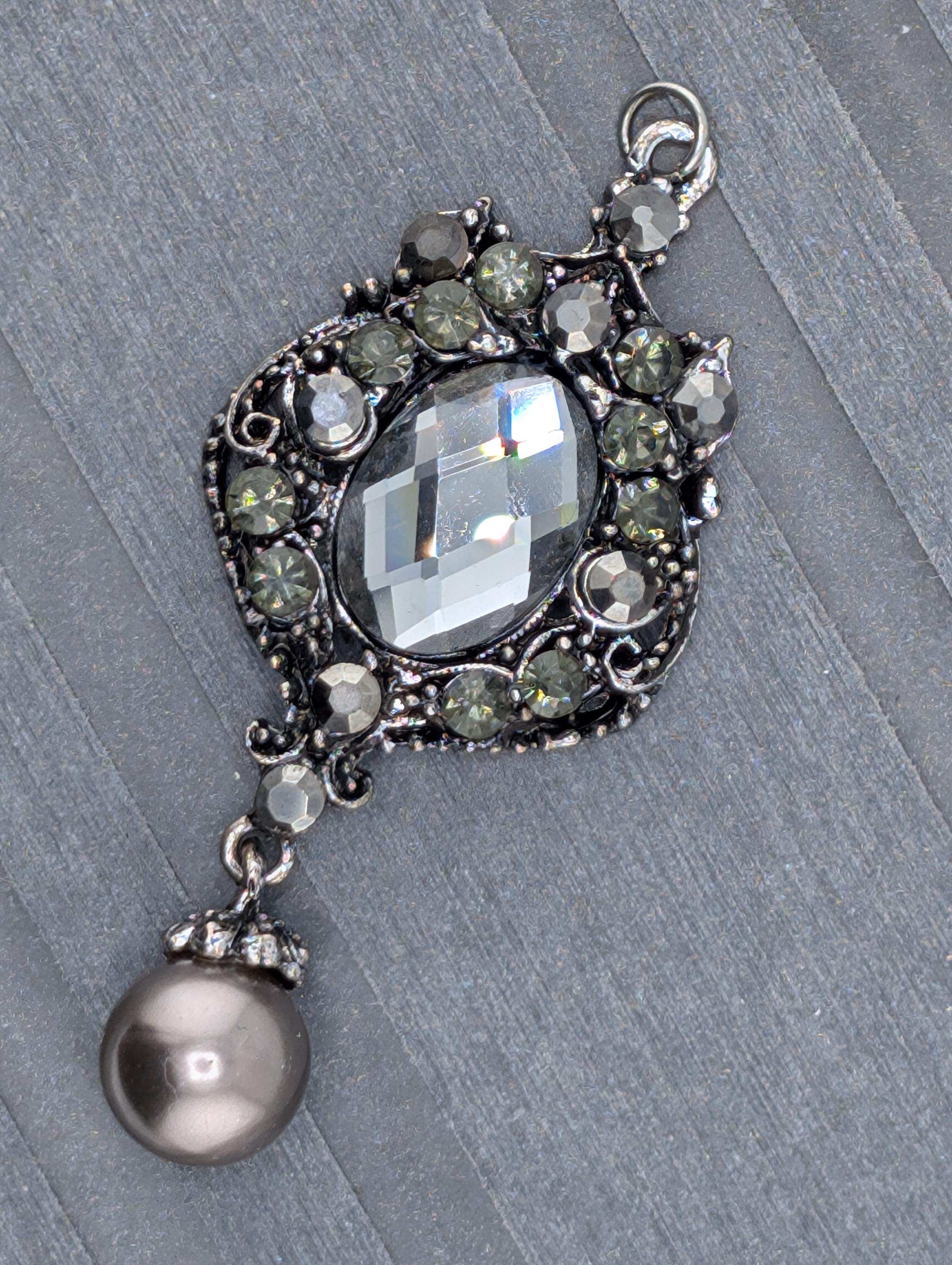 A silver-toned earring with a large crystal stone and a pearl-like accent piece, set against a gray background.