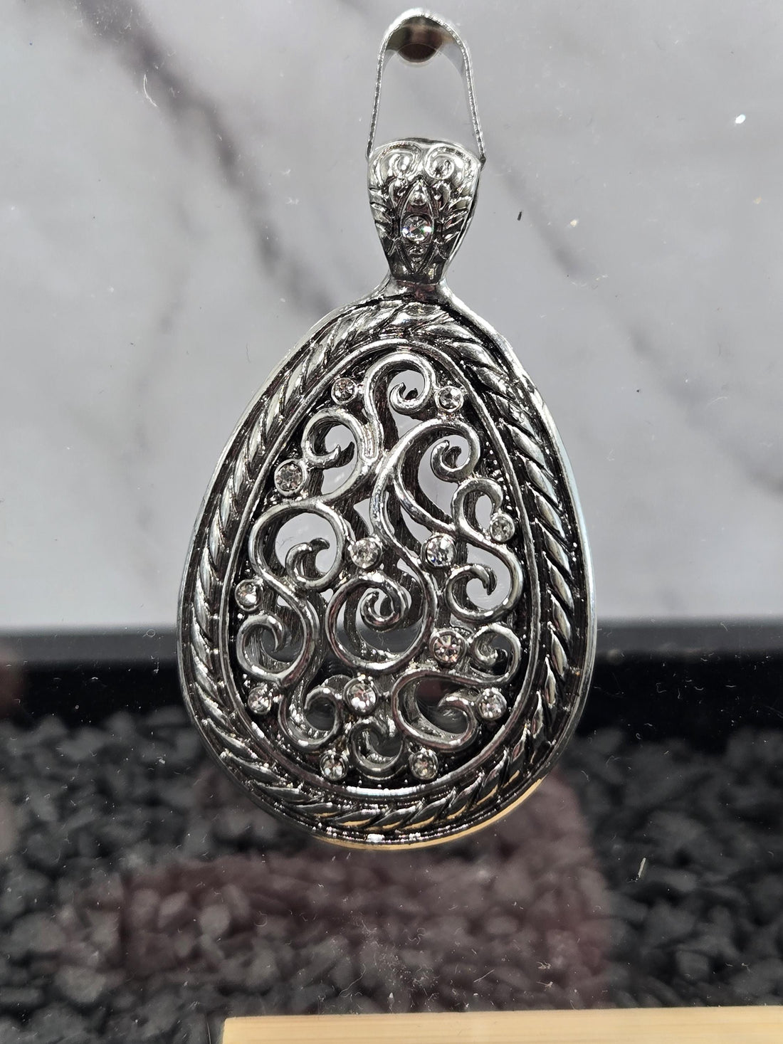 A close-up image of a decorative metal pendant with intricate designs and sparkling crystals.