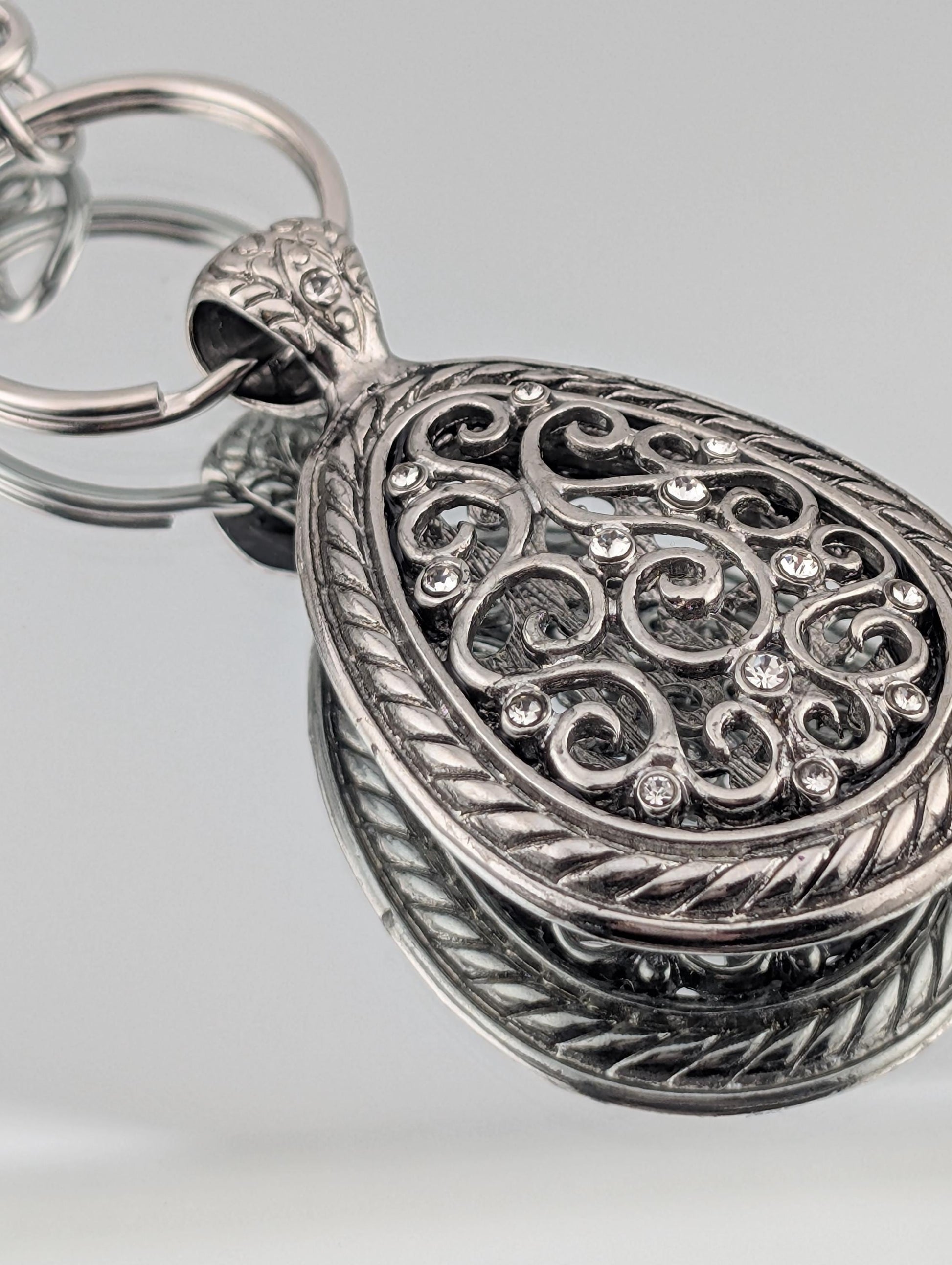 A silver-colored pendant with an intricate, decorative design and small rhinestones or crystals embedded in it.