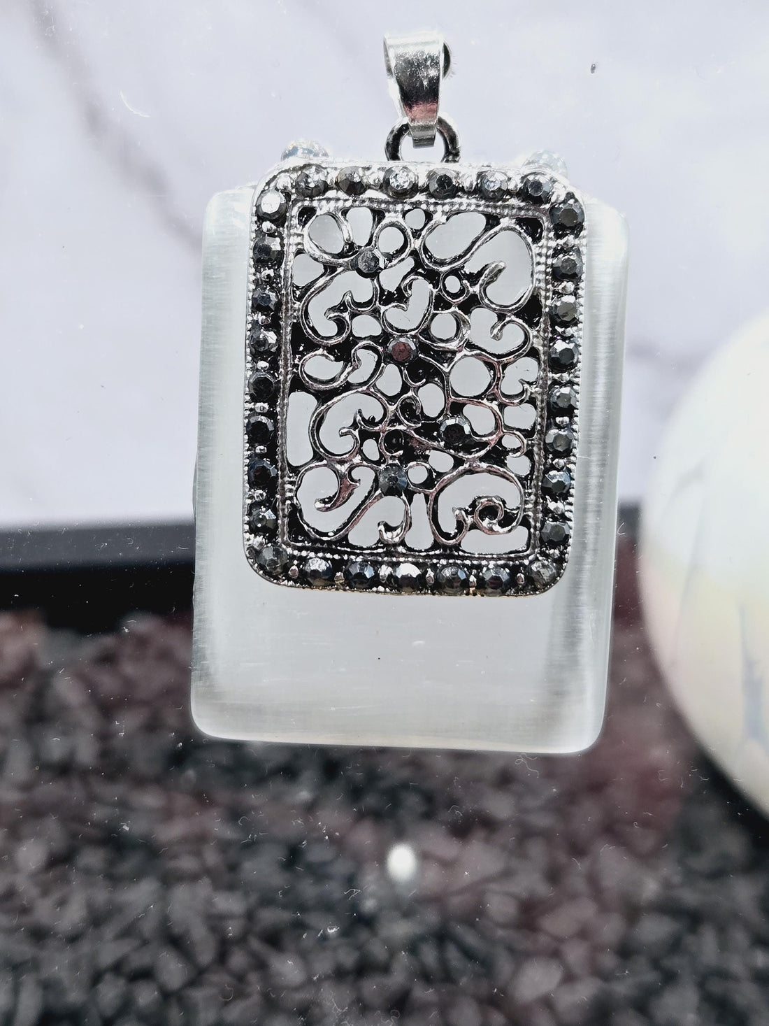 a pendant with a decorative metal design and a glass component, both adorned with small, sparkling stones.