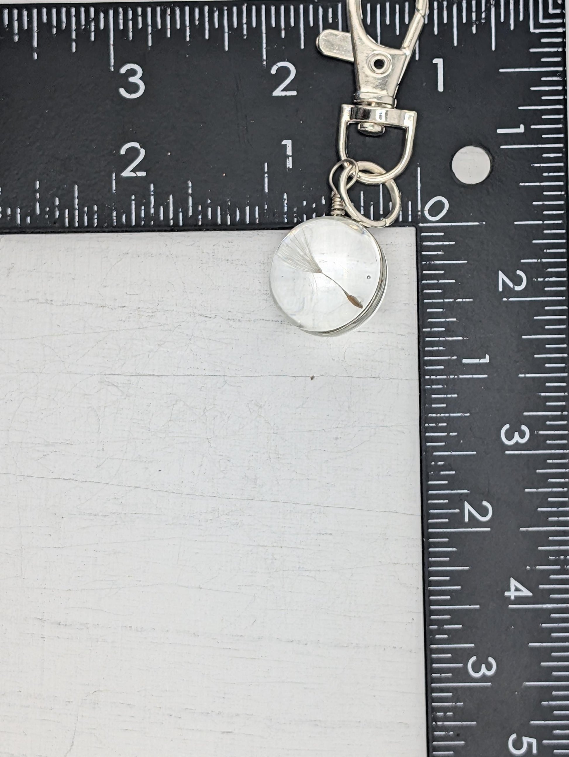 A silver keychain with a clear pendant is placed on a ruler, which is marked with inches and centimeters.