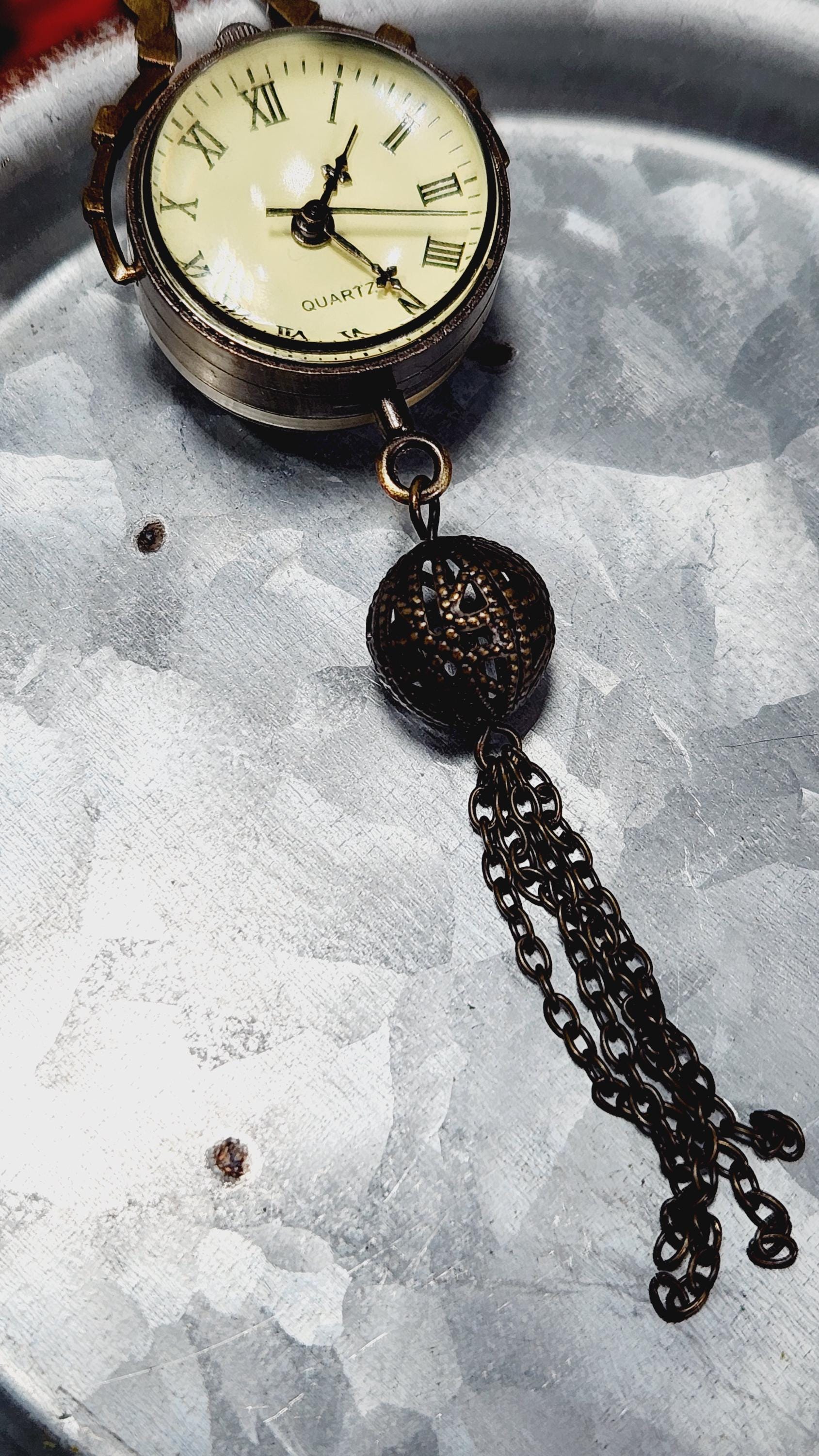 An old-fashioned pocket watch with a chain and a round ball attached to it, resting on a metal surface.