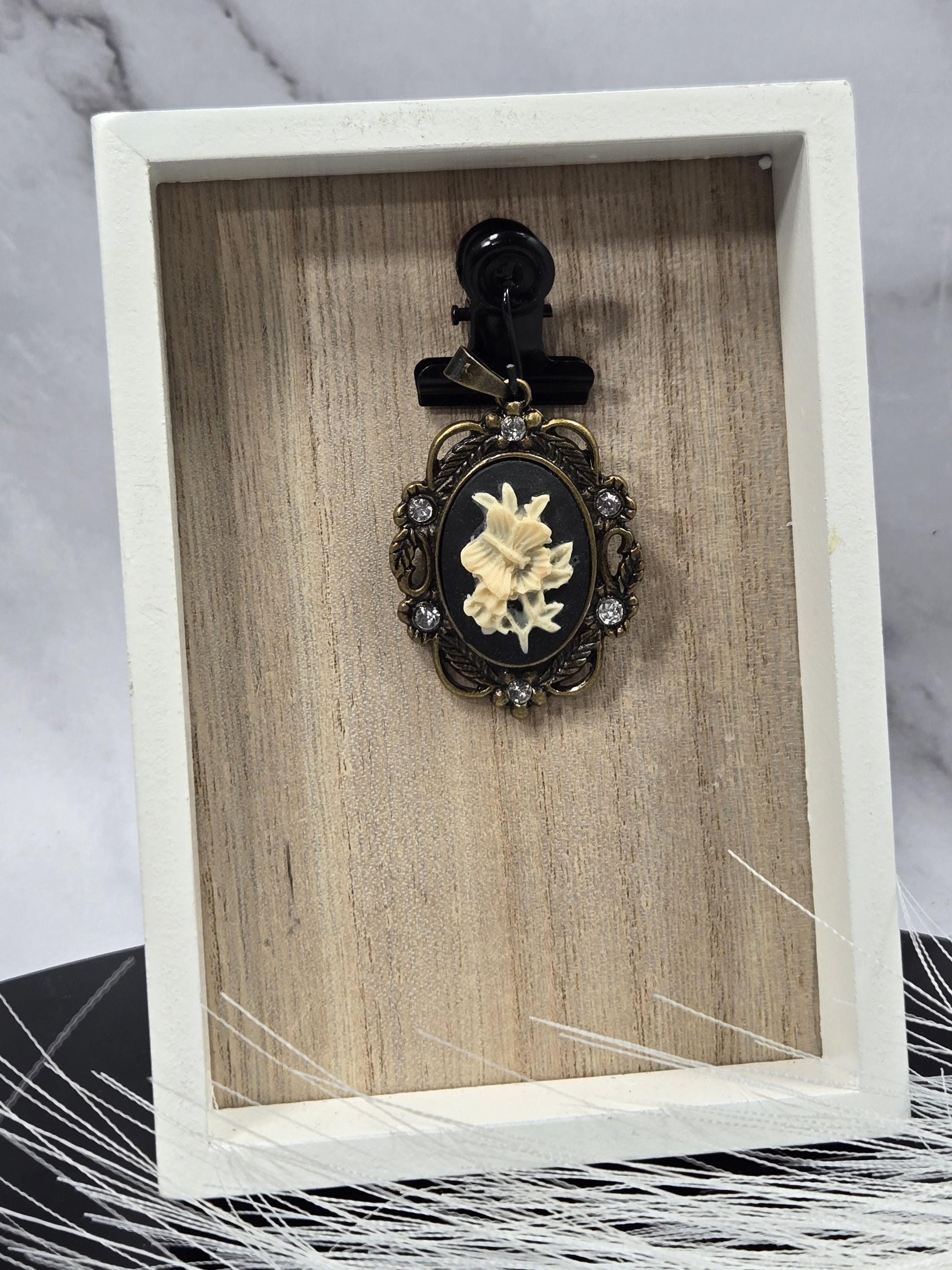 A white wooden box with a black clasp and a decorative brooch with a floral design on it.