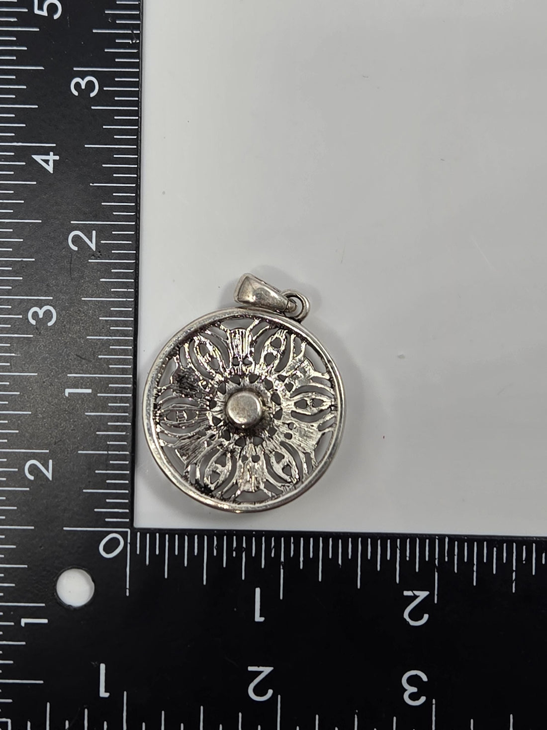 A silver pendant with an intricate design, featuring a central motif surrounded by smaller, symmetrical patterns.