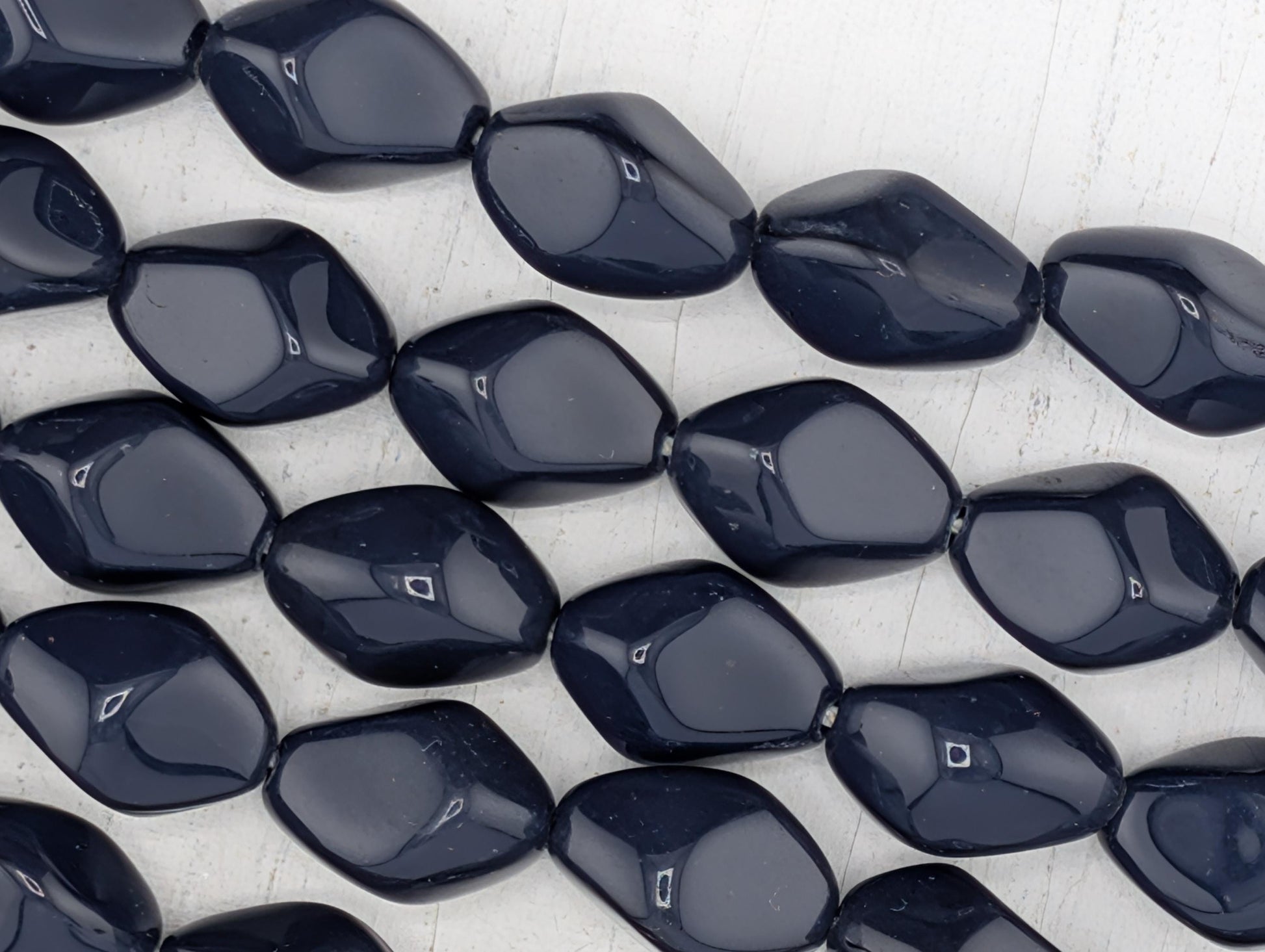 a collection of dark blue, irregularly shaped beads arranged in a grid-like pattern on a white background.