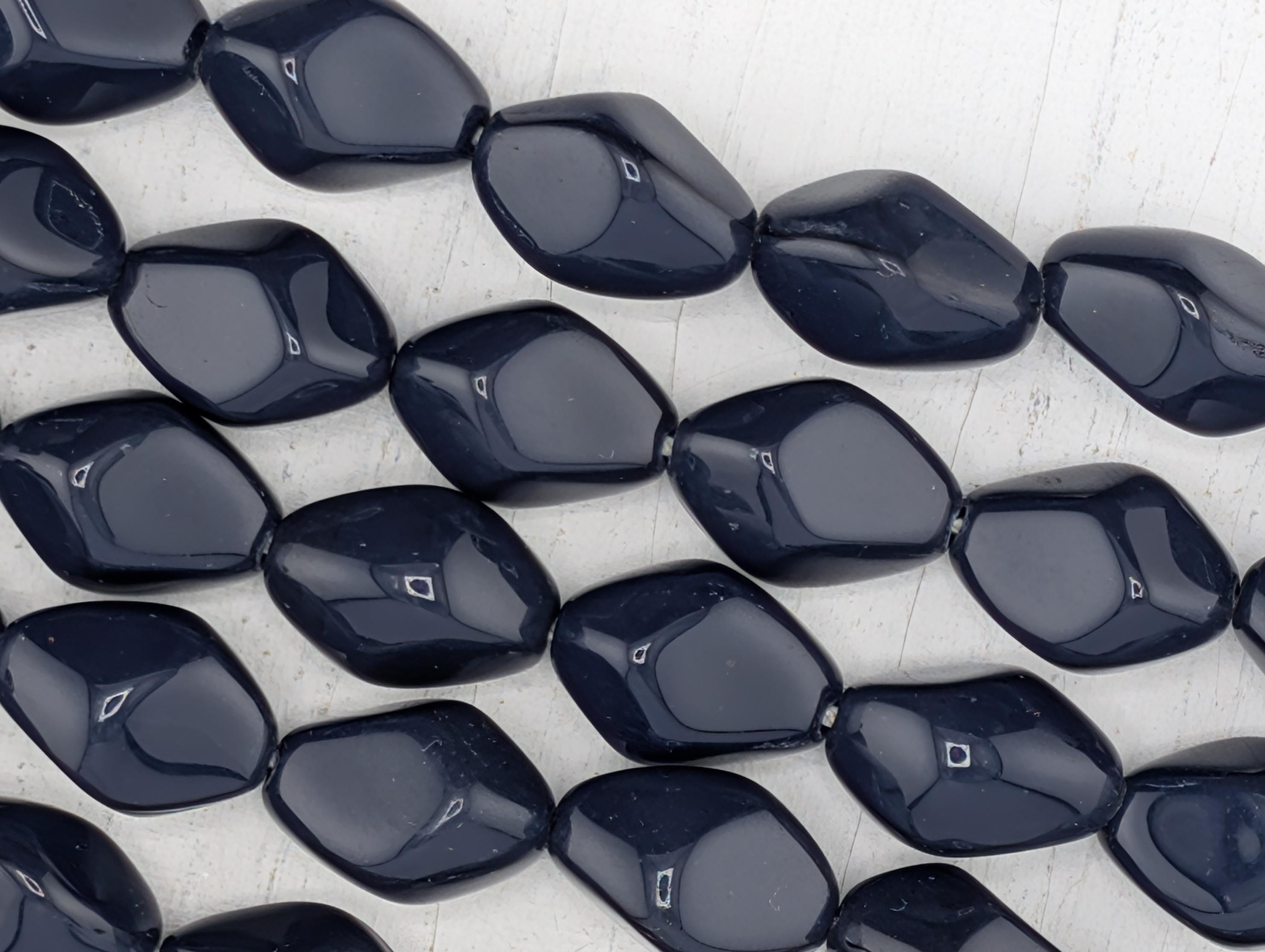 a collection of dark blue, irregularly shaped beads arranged in a grid-like pattern on a white background.