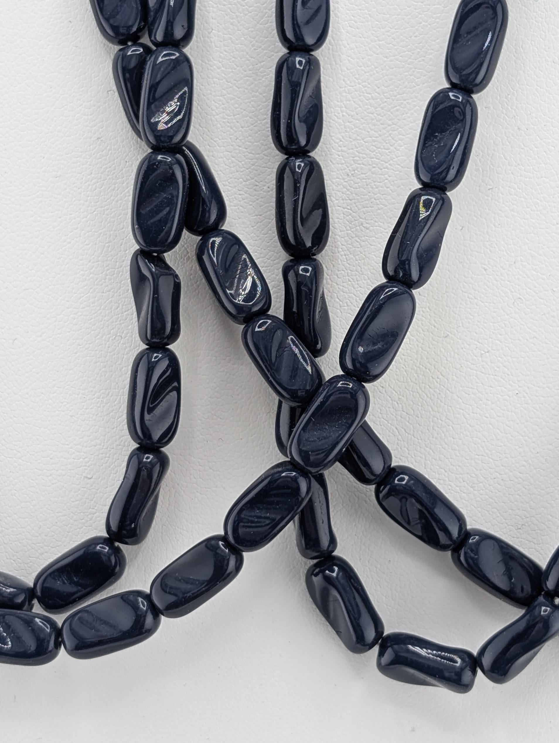 A close-up image of a collection of dark blue beads arranged in a tangled, overlapping pattern.