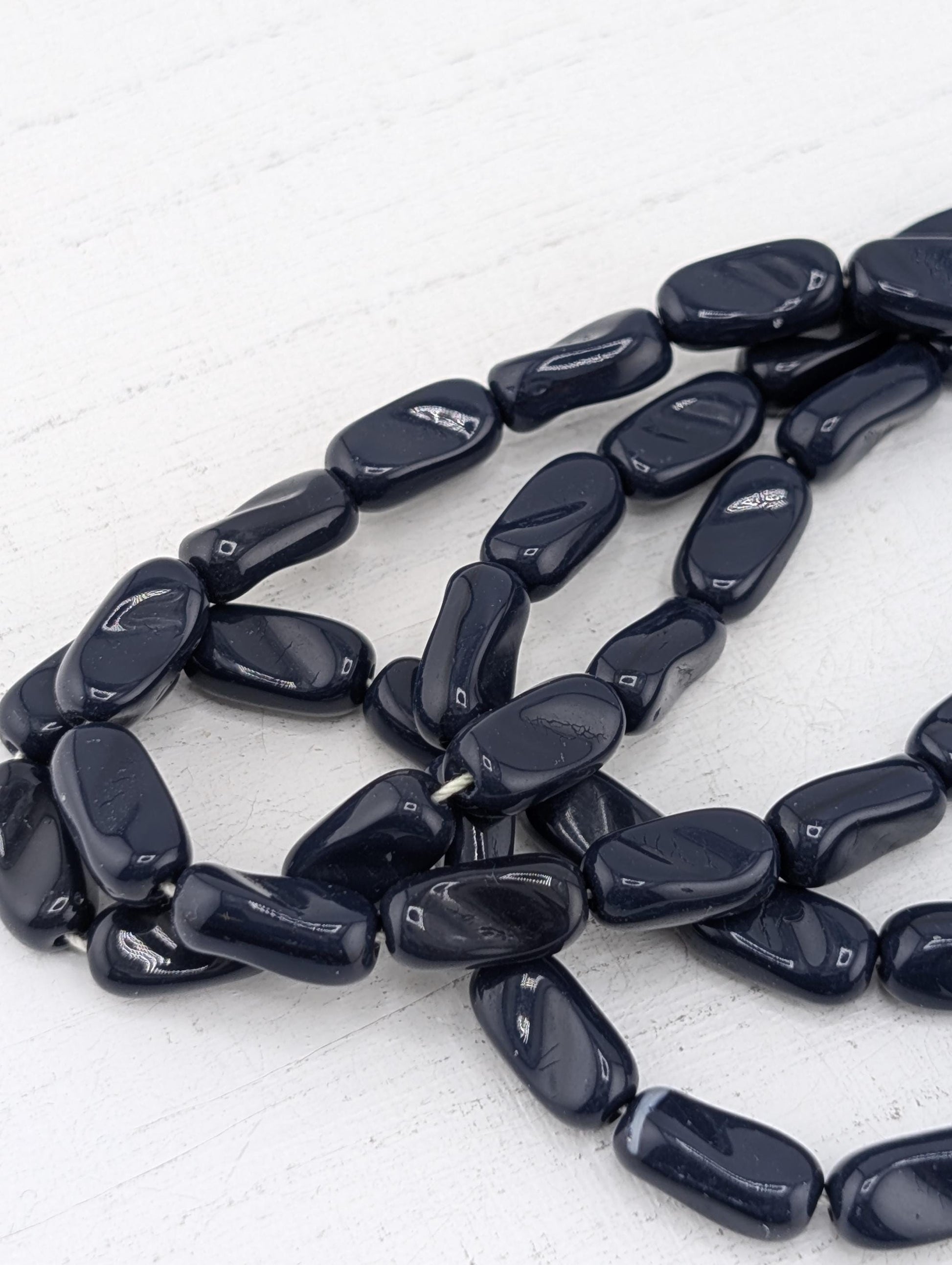 A collection of dark blue beads arranged in a loose, tangled pattern on a white surface.