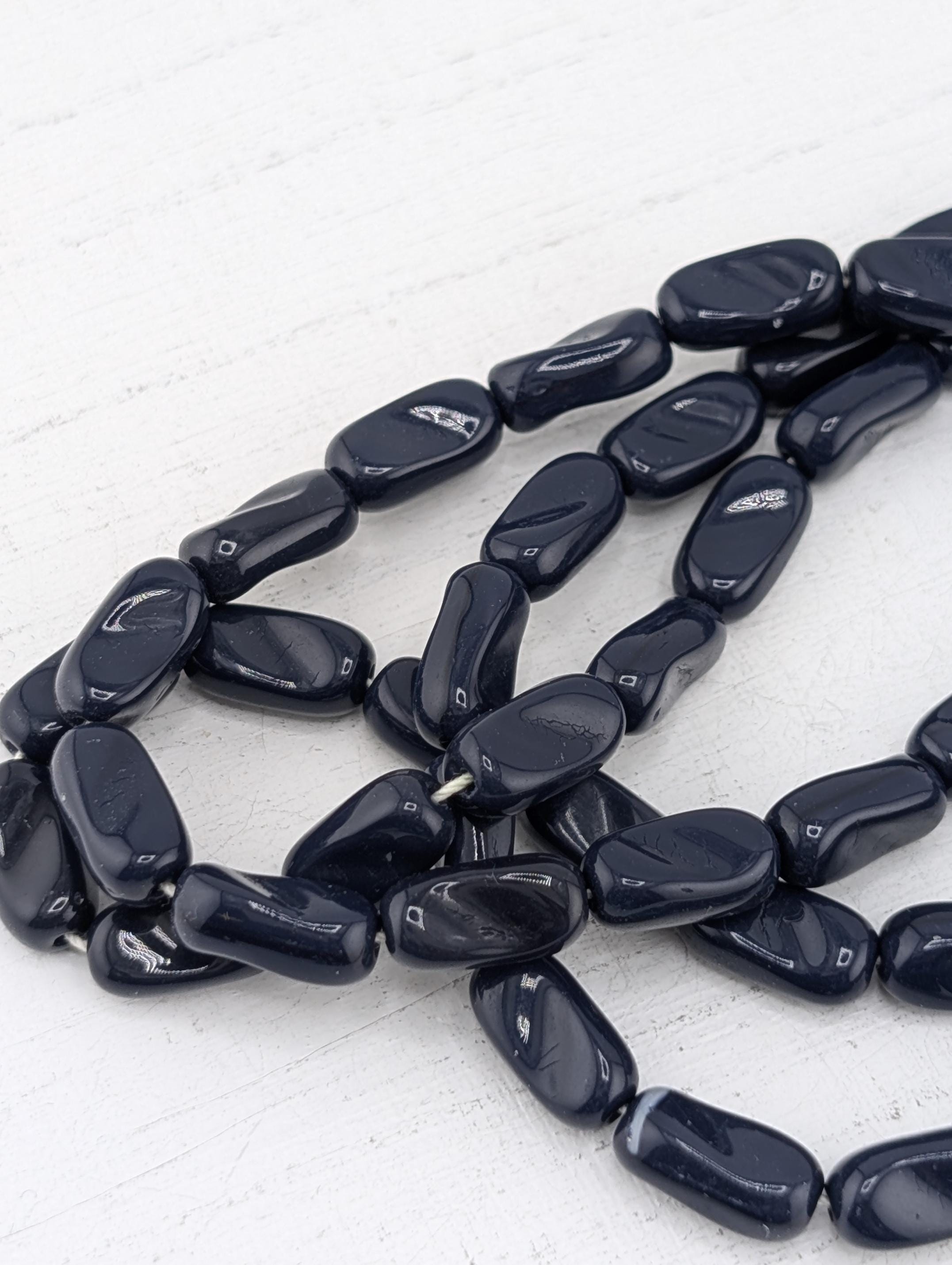 A collection of dark blue beads arranged in a loose, tangled pattern on a white surface.