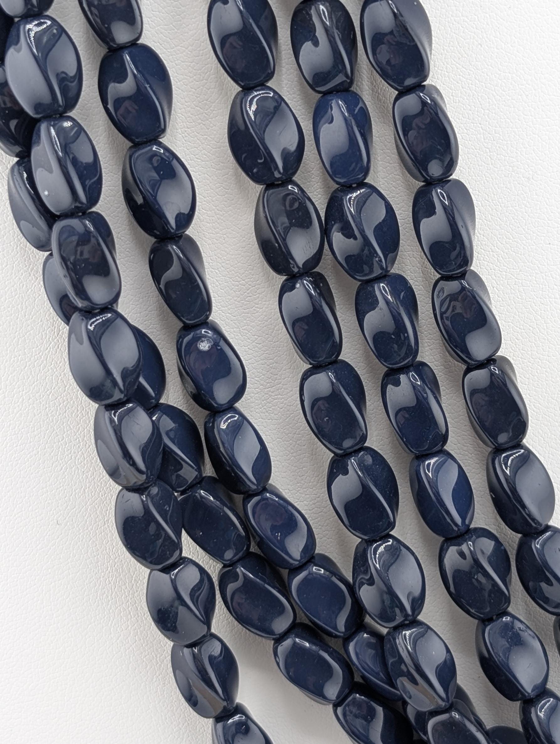 A close-up image of a collection of dark blue beads arranged in a row, with a white background.
