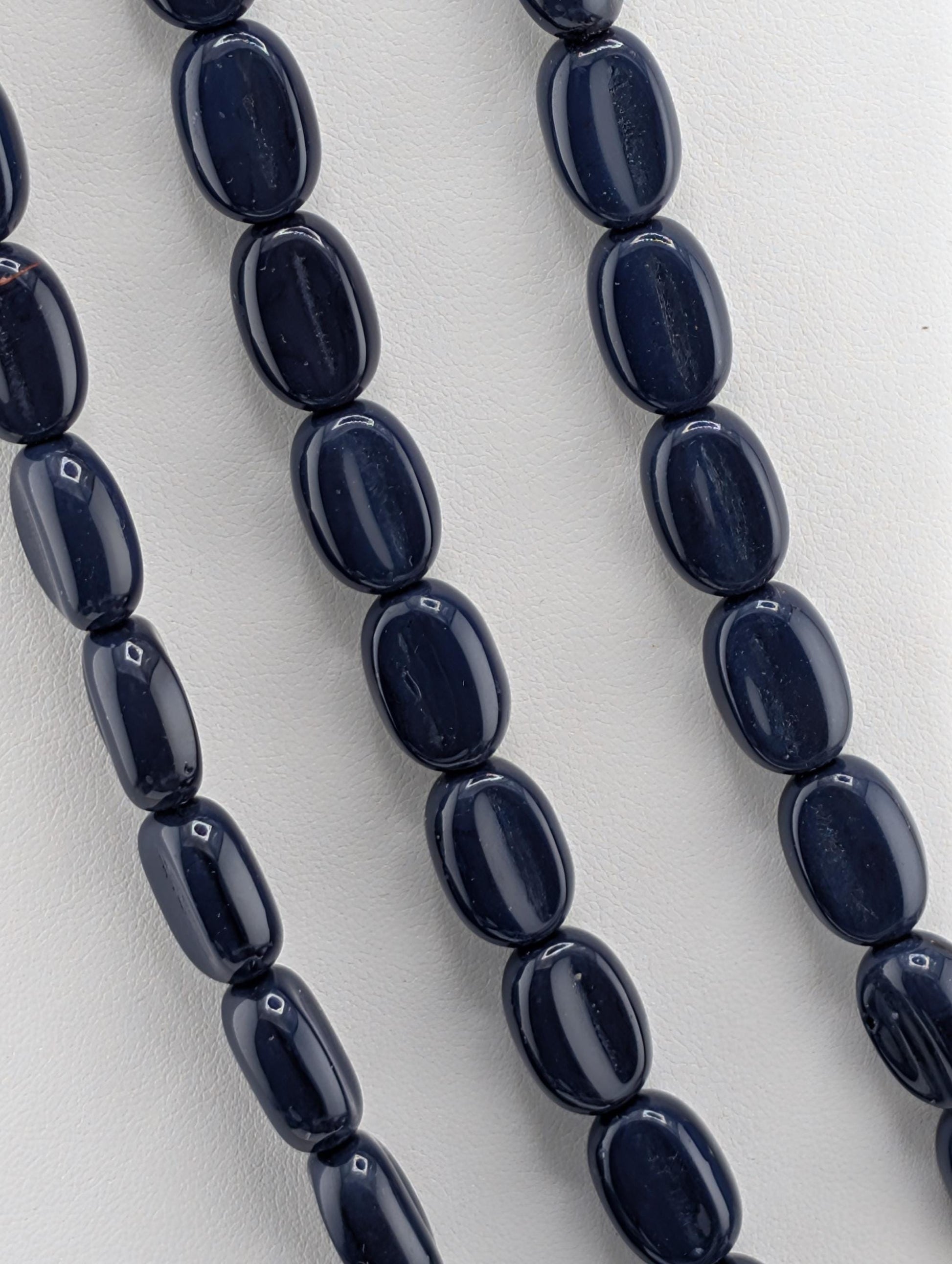a close-up view of a collection of dark blue beads arranged in a row, with a white background.