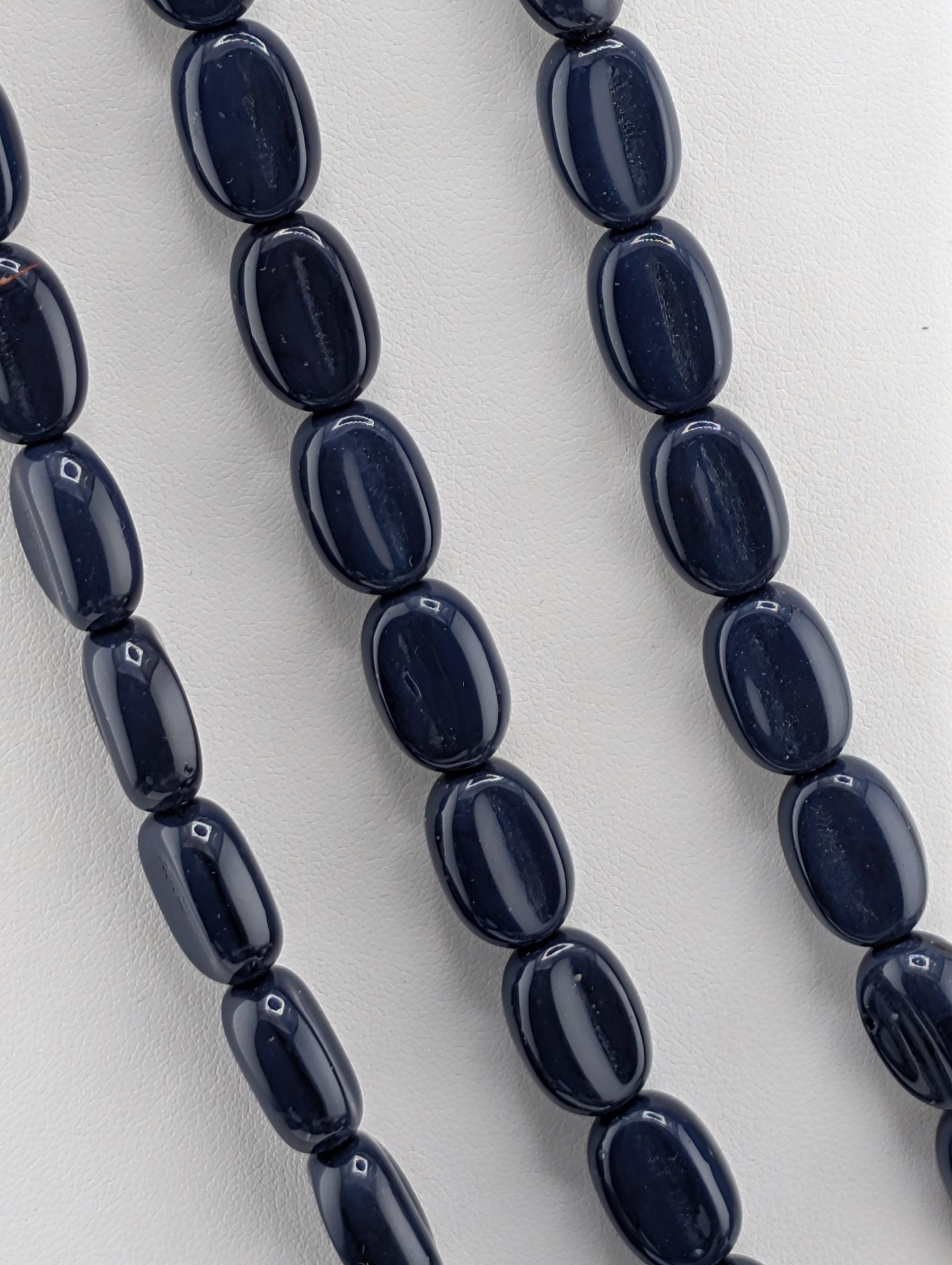 a close-up view of a collection of dark blue beads arranged in a row, with a white background.