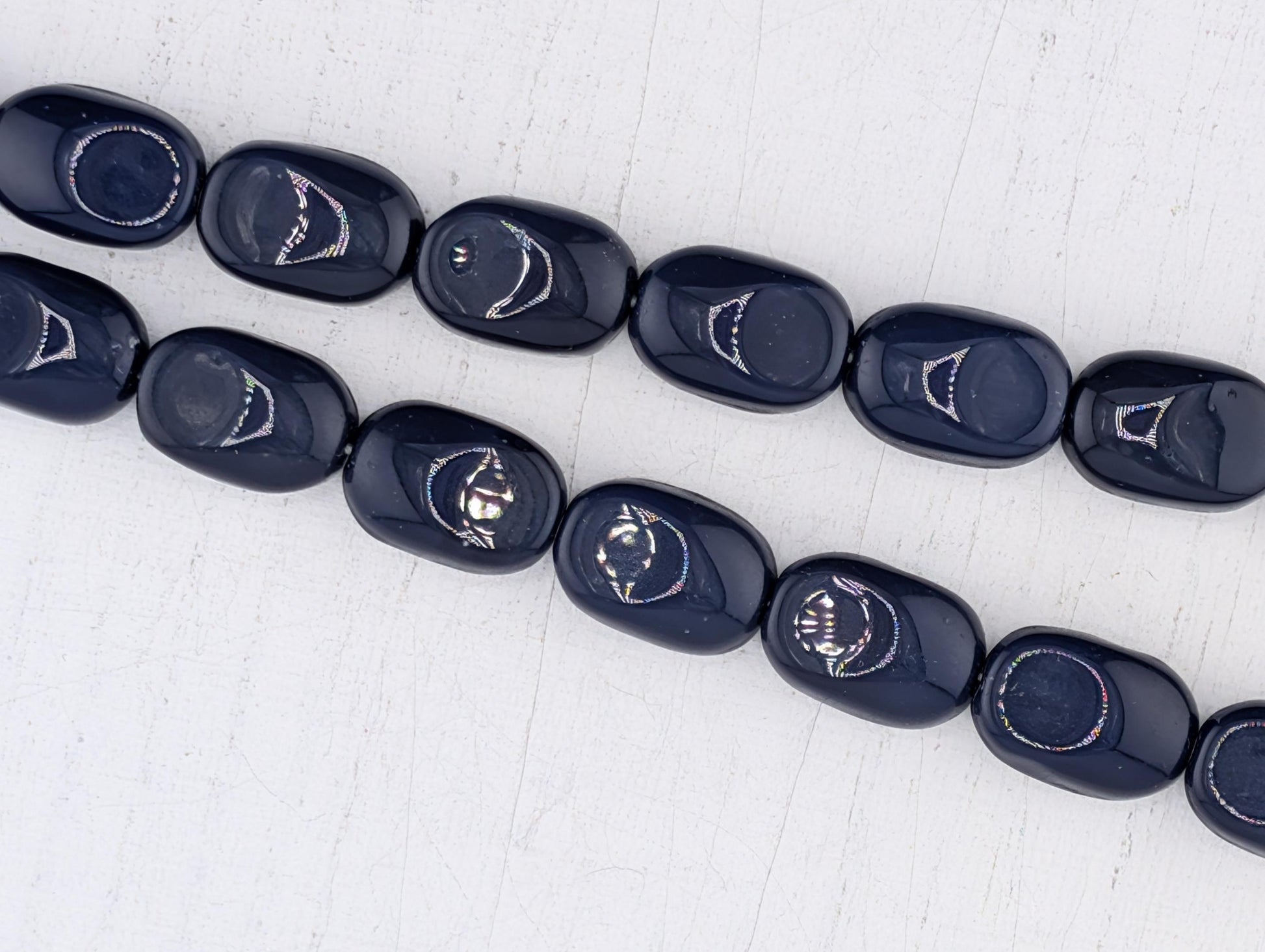 A row of dark blue beads with a pattern of smiling faces on them, arranged on a white surface.