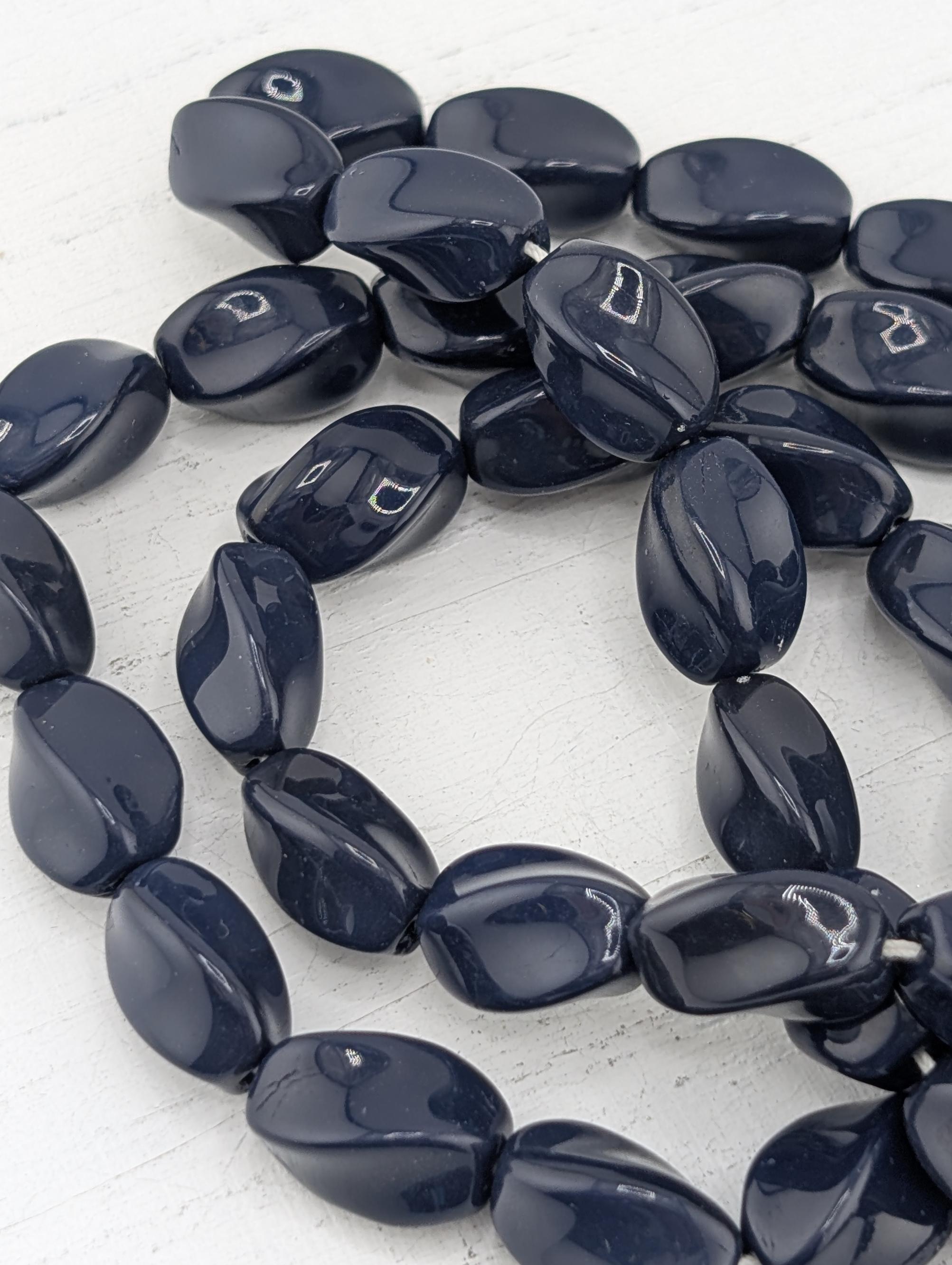 A collection of dark blue, irregularly shaped beads arranged in a circular pattern on a white surface.