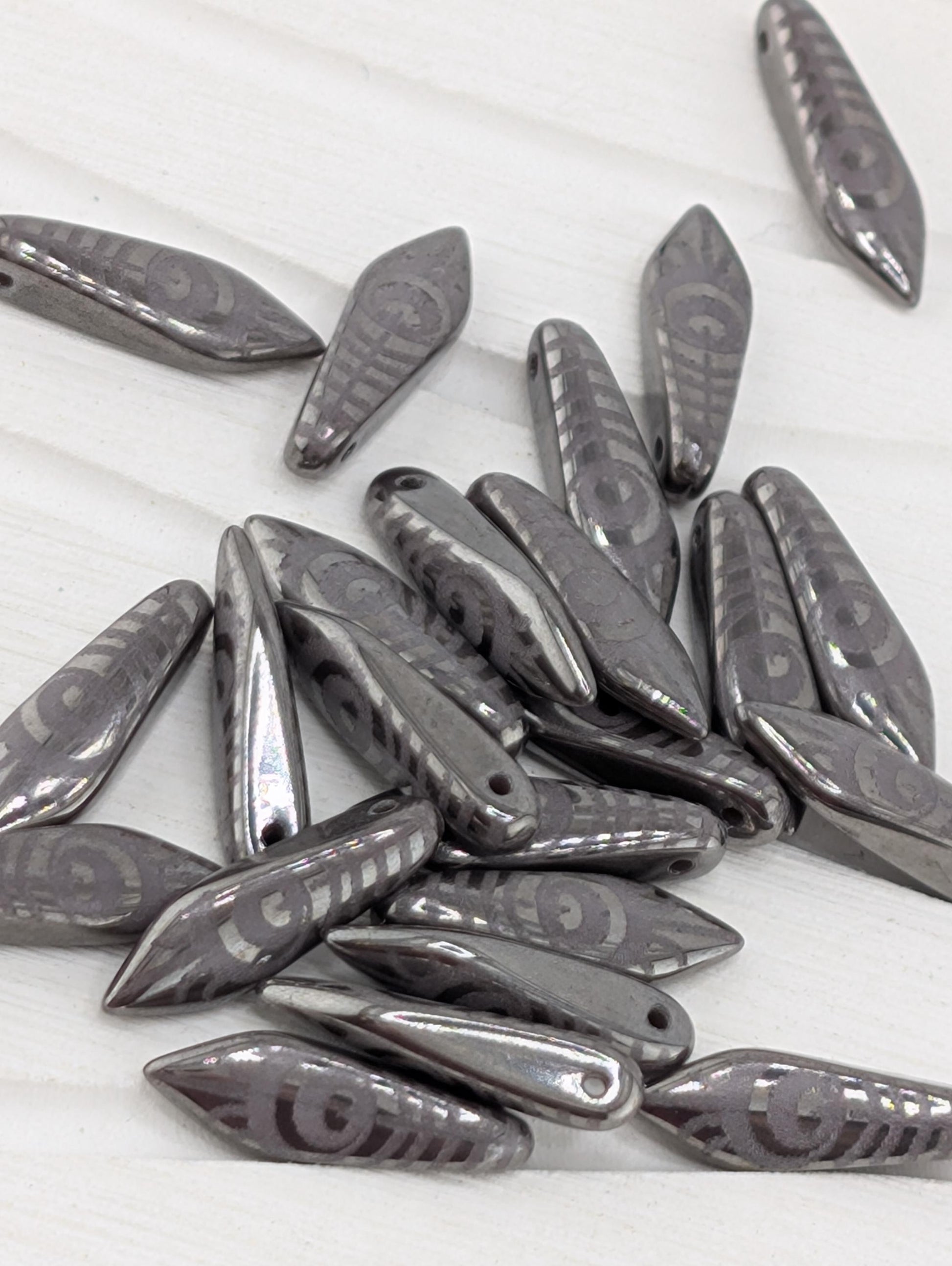 a collection of metallic beads or charms with a repeating pattern of circles or other geometric shapes, scattered on a white surface.