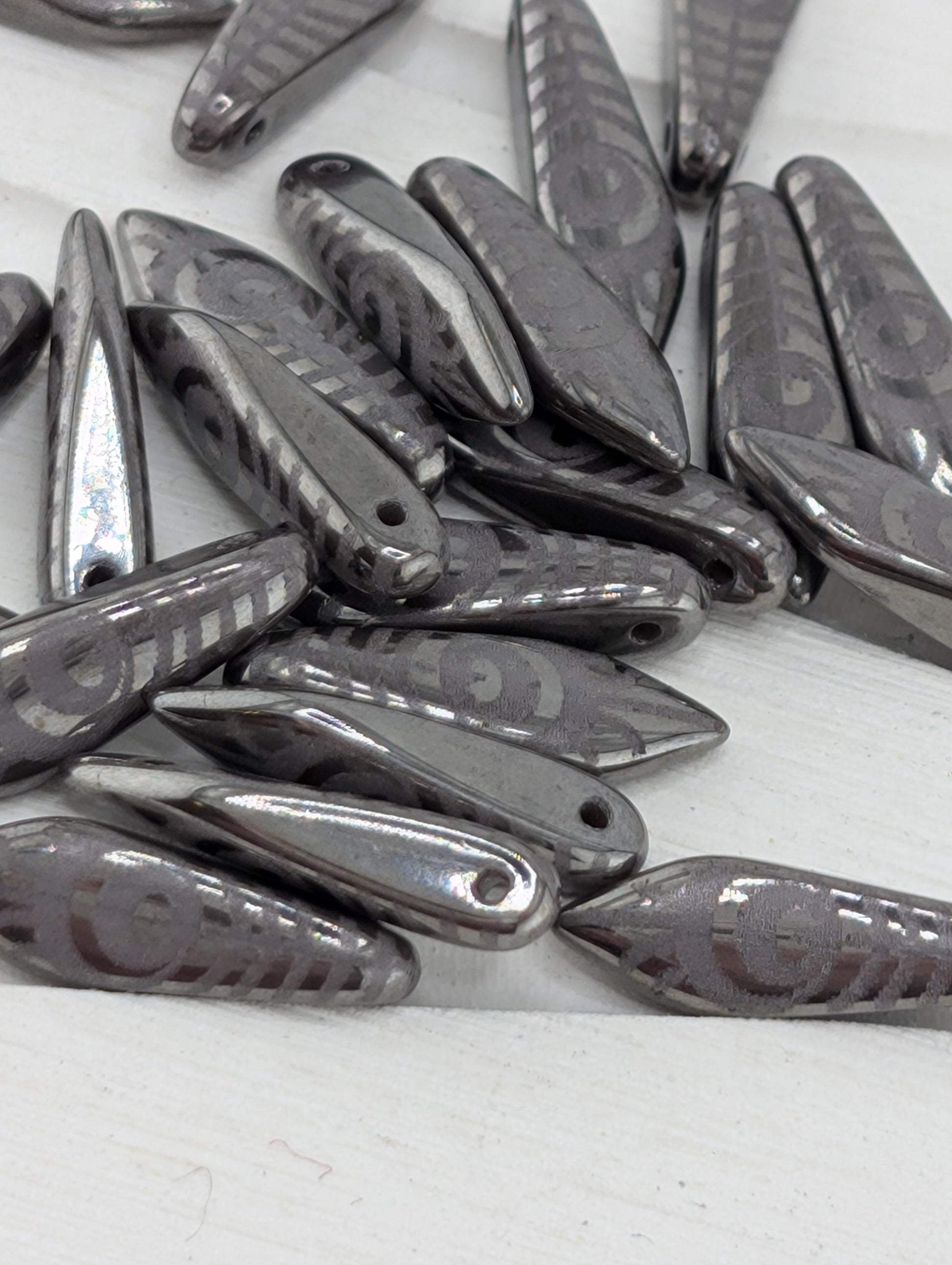 a collection of metallic beads or charms with a repeating pattern of circles or other geometric shapes, arranged on a white surface.