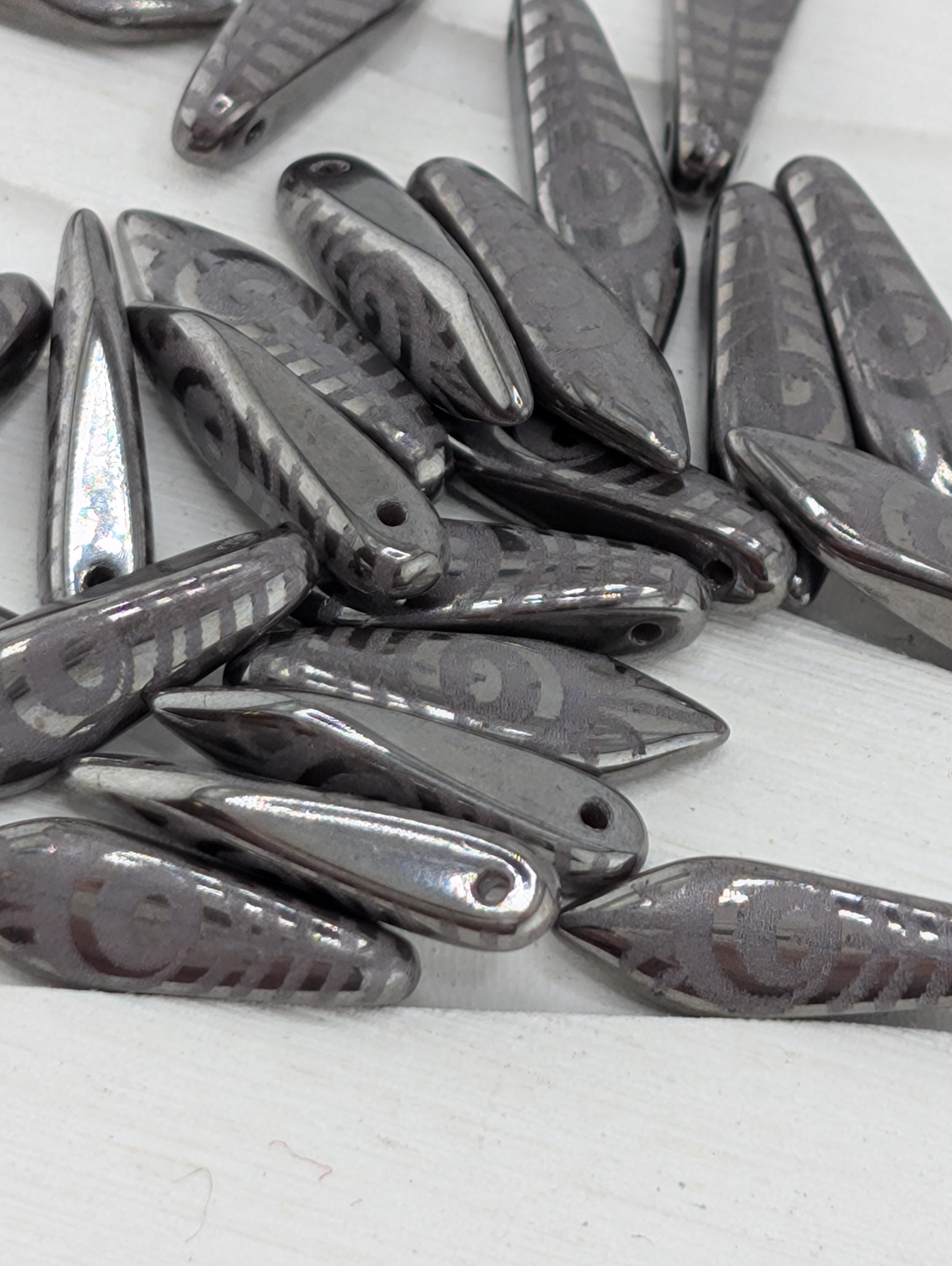 a collection of metallic beads or charms with a repeating pattern of circles or other geometric shapes, arranged on a white surface.